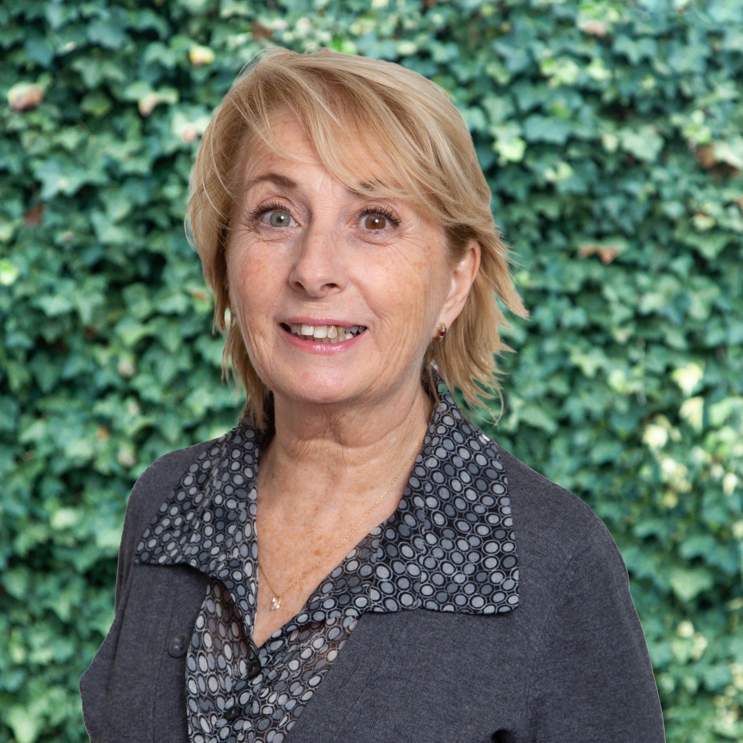 Smiling woman in dark sweater in front of leafy background.