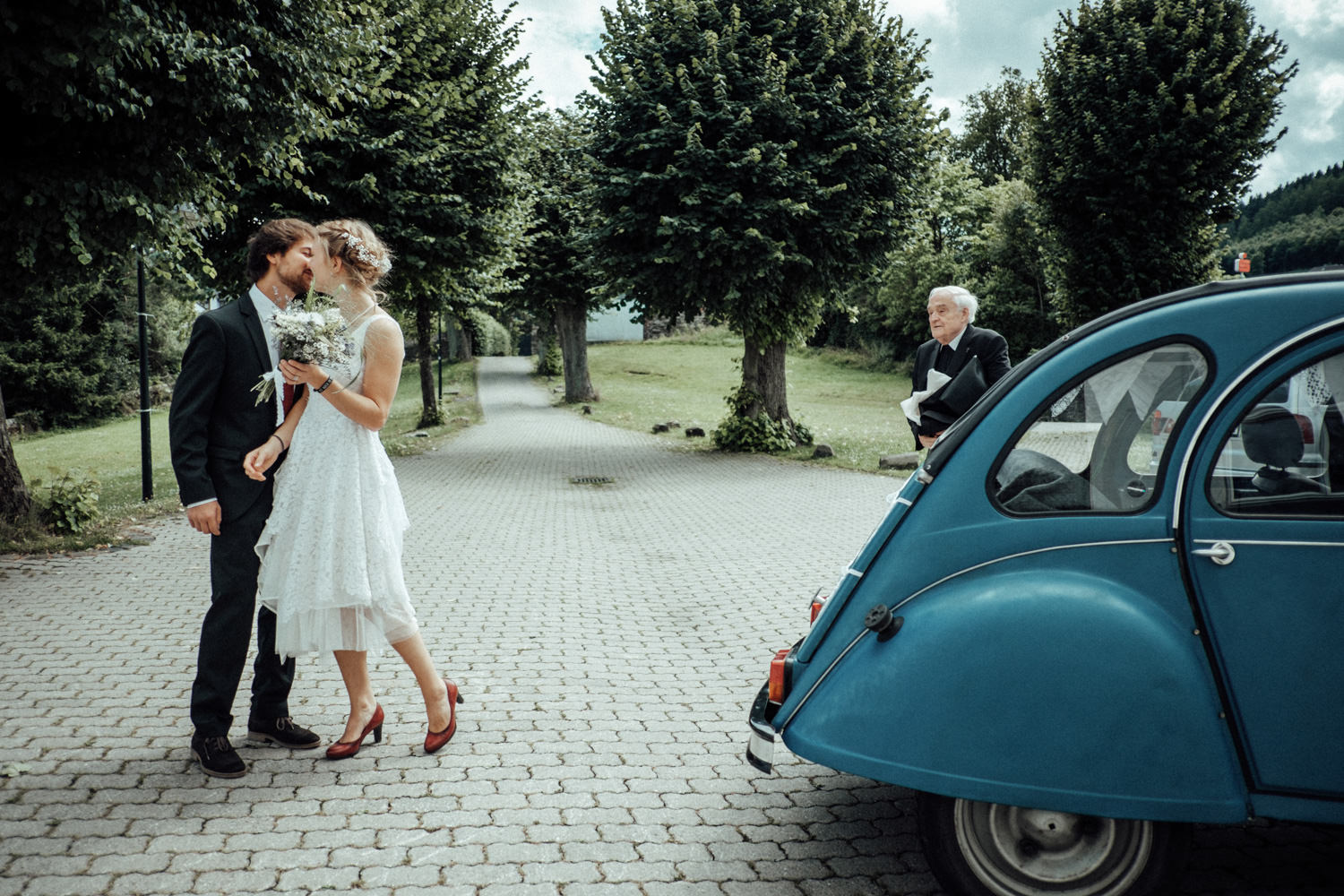 Das Brautpaar küsst sich neben Ente als Oldtimer-Hochzeitsauto