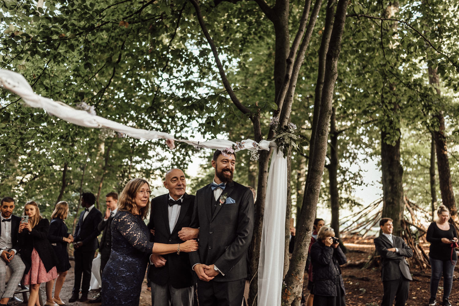 Gerührter Bräutigam mit seinen Eltern bei Anbetracht seiner wunderschönen Braut bei der freien Waldhochzeit nahe Köln