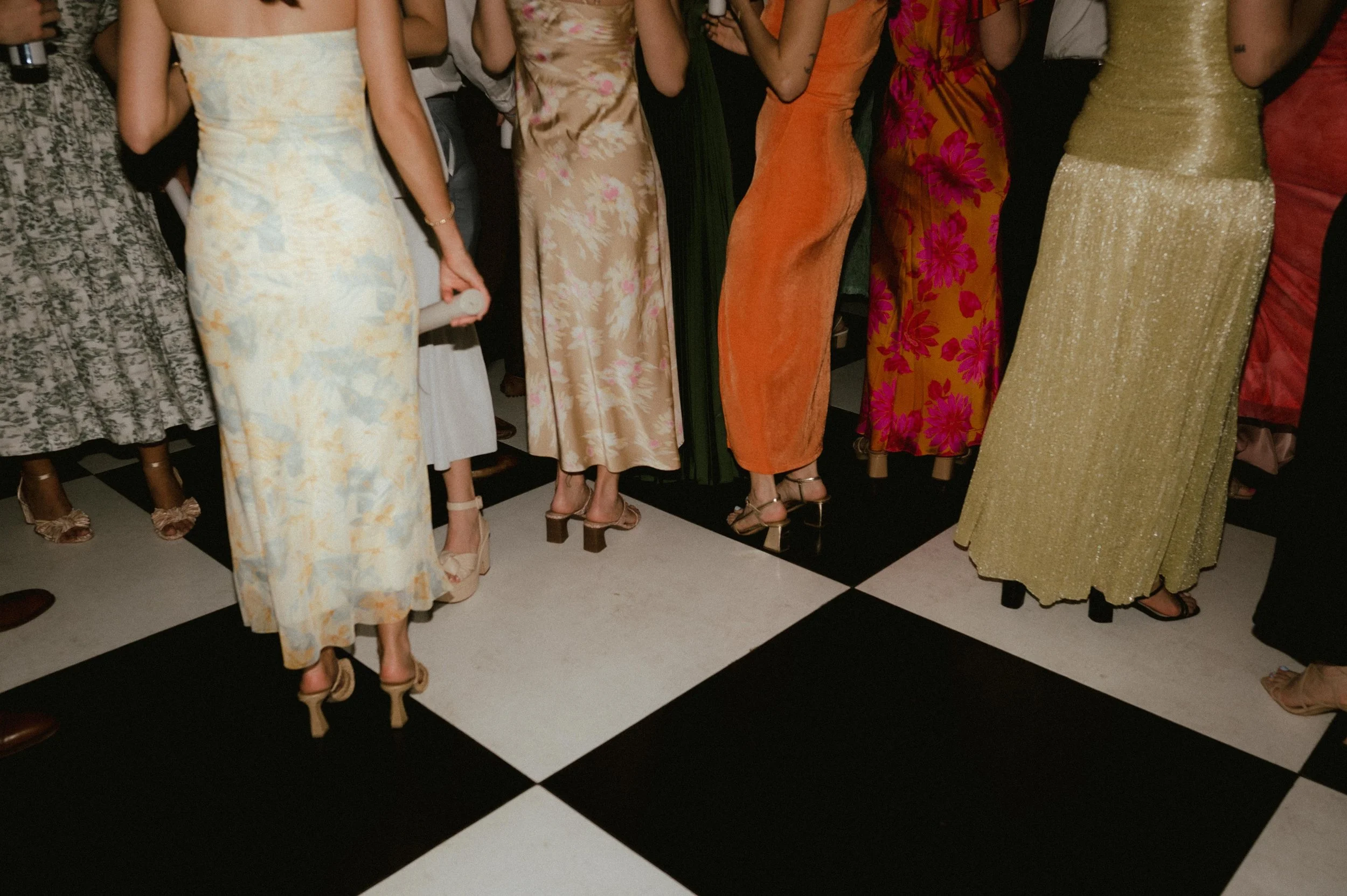 A black and white checked dance floor at Mallard's Croft in Memphis Tennessee, with women in yellow, orange, pink, gold, and green dresses and high heels dancing. The photo is cut off at the shoulders and shows only the wedding guest dresses.