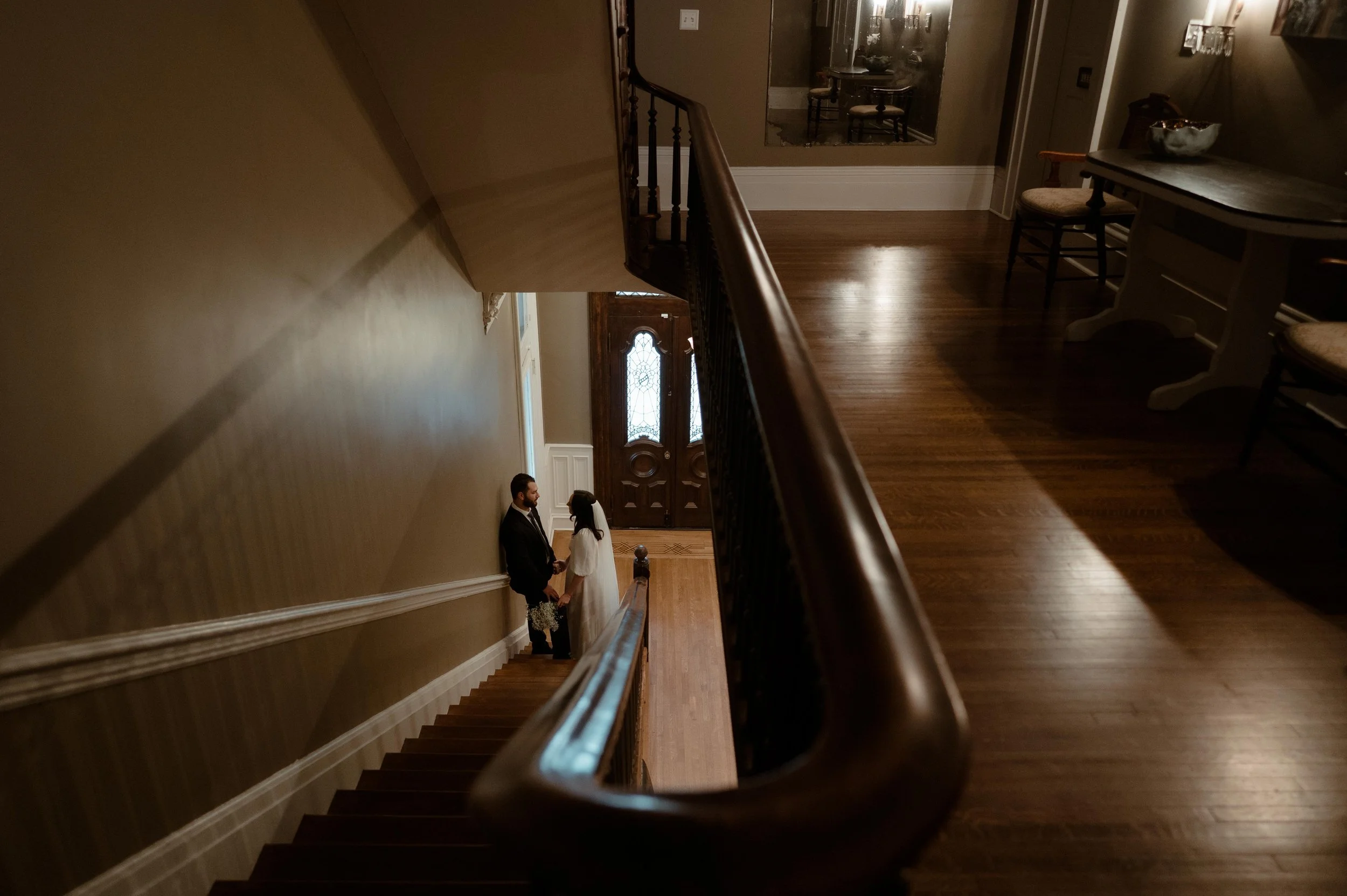 A couple poses on the staircase at the James Lee House in Memphis, Tennessee. The couple is small in the photo, framed by the second floor balcony and the staircase.