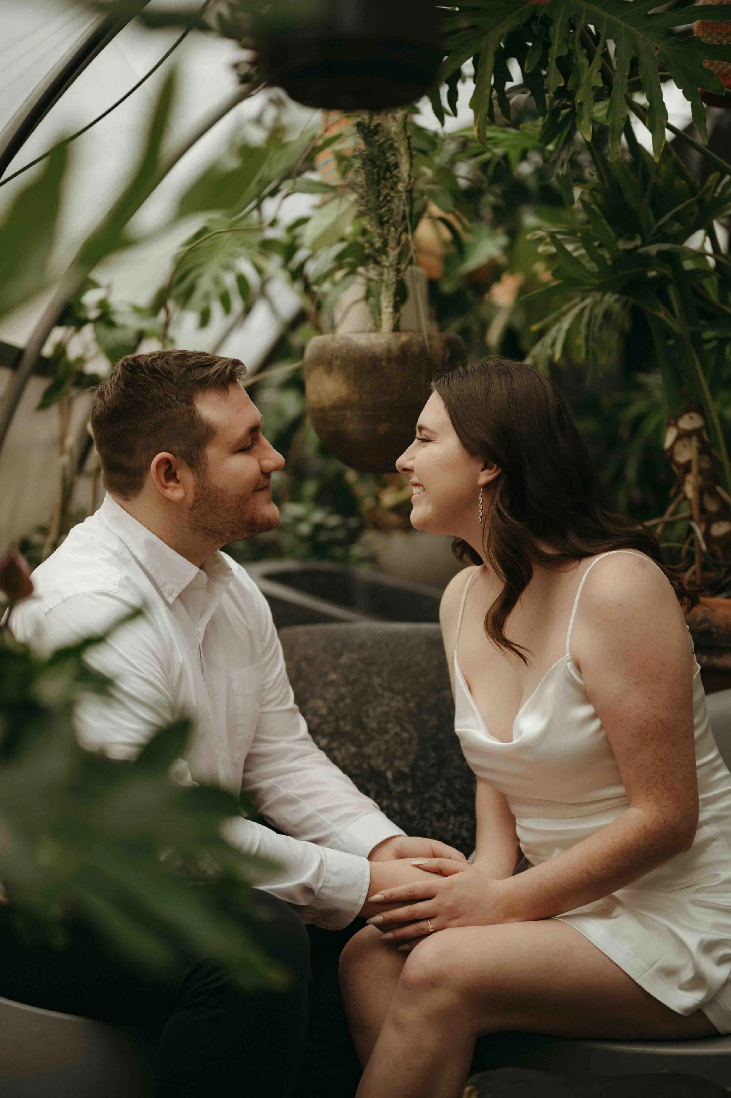 Engagement photo of a couple dressed in white smiling at each other sitting in the Greenhouse Bar in Nashville, Tennessee.