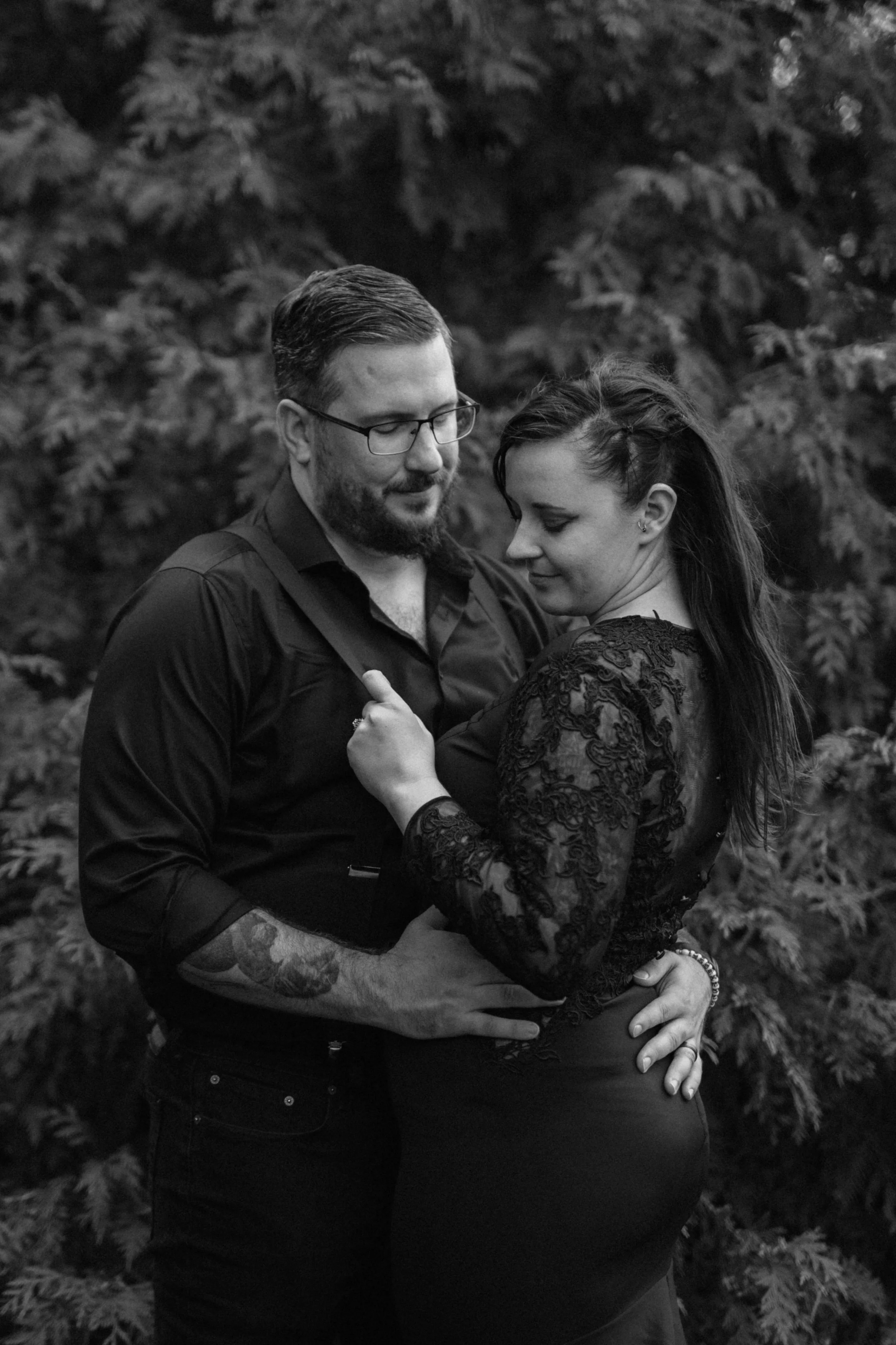 Black and white moody bridal portrait of a couple holding each other in front of foliage.