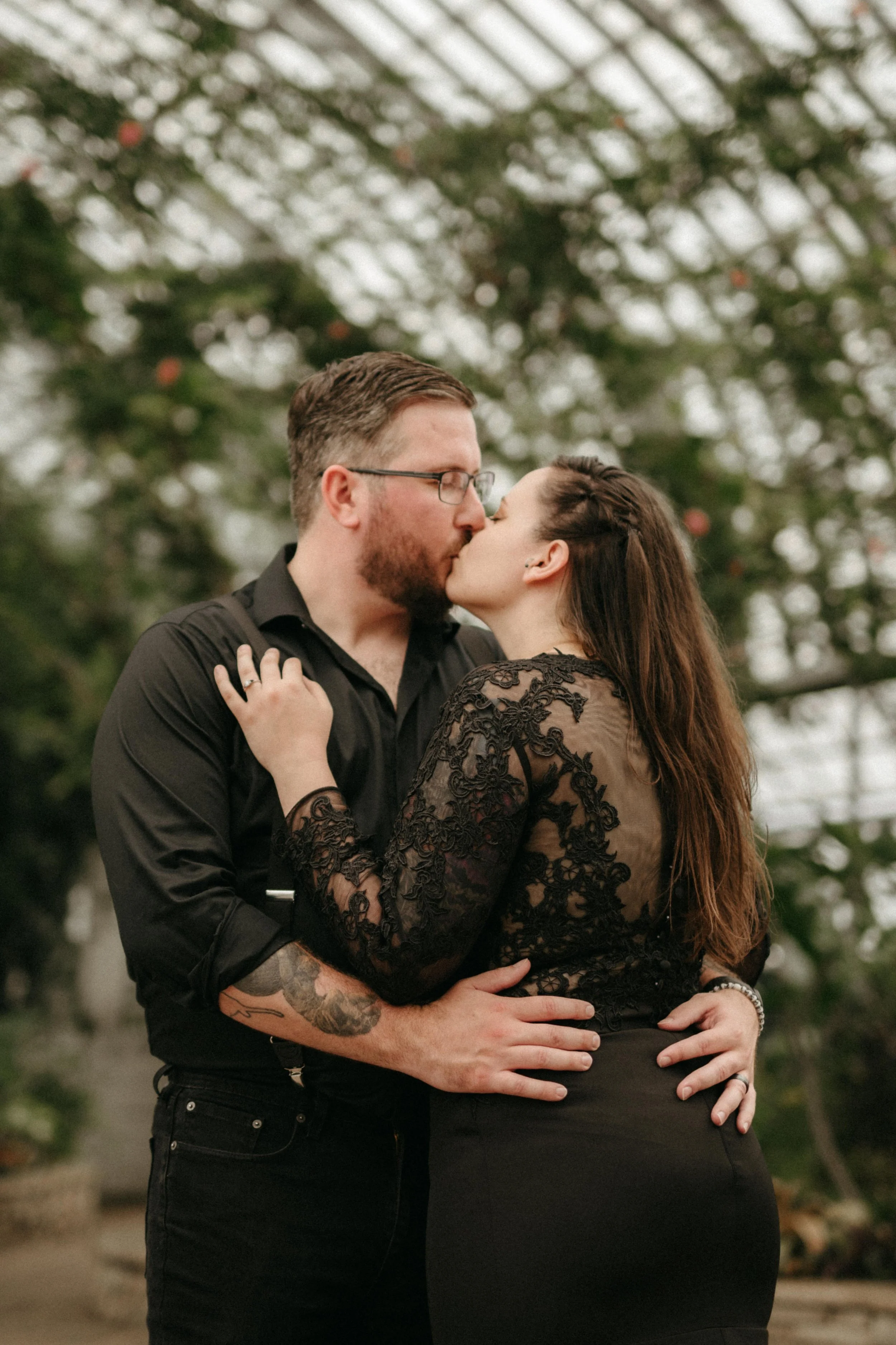 Moody bridal portrait of a bride and groom wearing all black and kissing and embracing.
