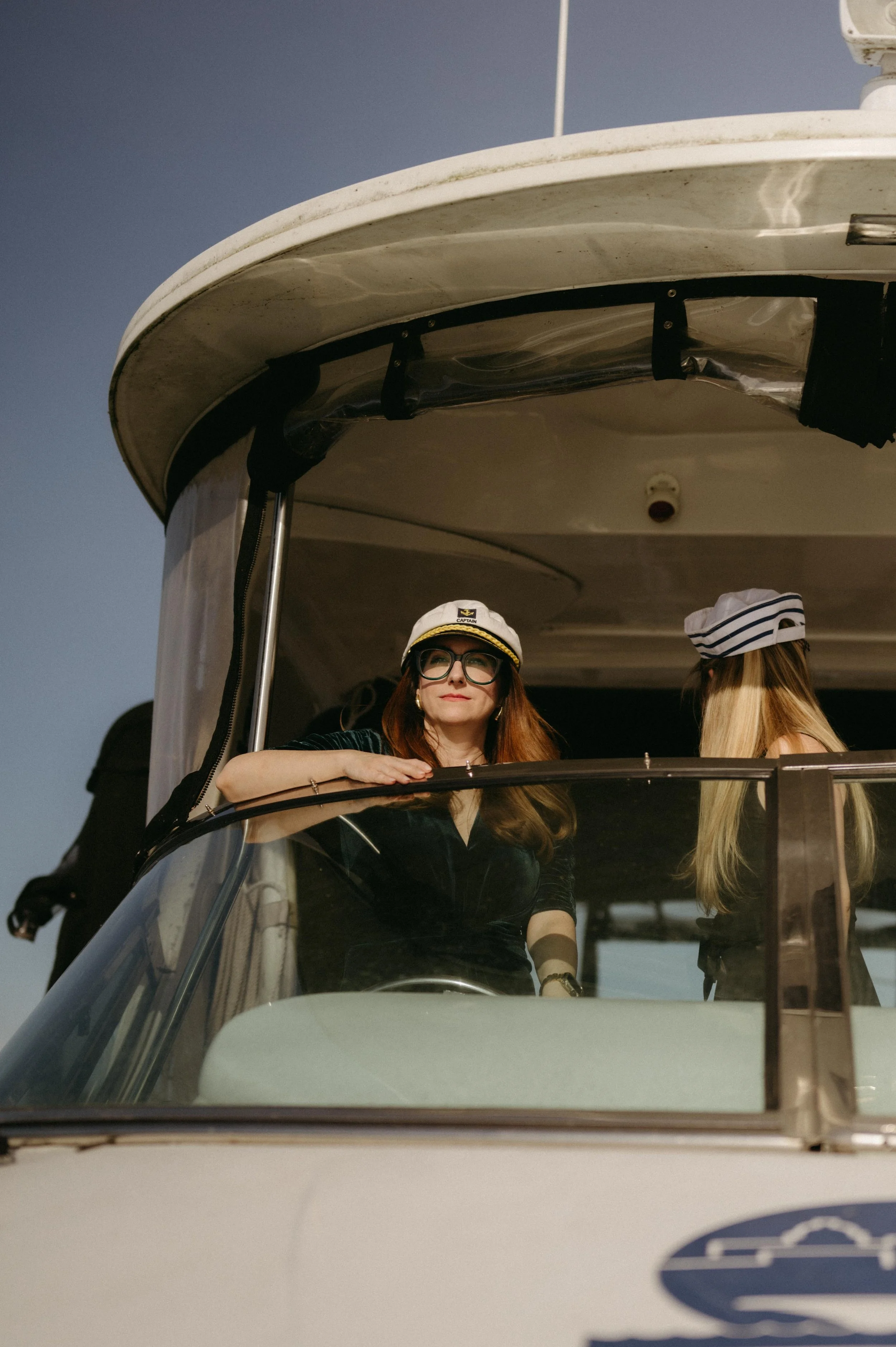Wedding guests take turns steering the boat on a rehearsal dinner cruise around Lake Mendota. Moody Madison wedding photographer. Madison Wisconsin wedding photographer.