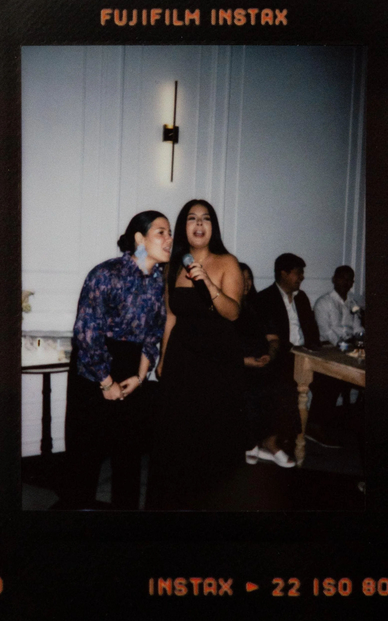 Instant film polaroid wedding photography two guests dressed in blue and black sing karaoke at a wedding reception in the Parisian in Huntsville, Alabama. Moody Huntsville wedding photographer. Documentary Huntsville wedding photographer.