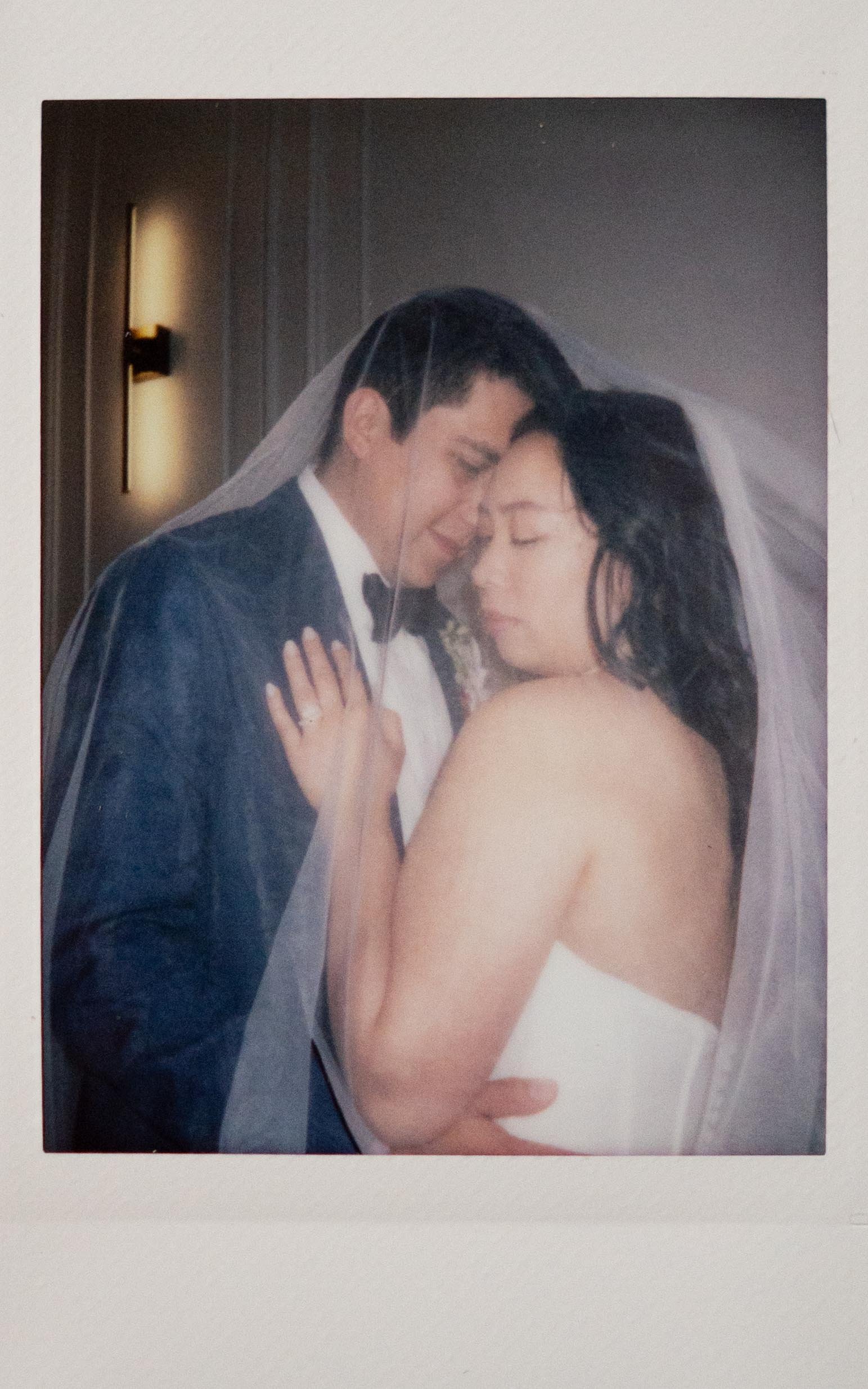 Polaroid photo of a bride and groom posing under a veil inside The Parisian in Huntsville, Alabama. The groom rests his forehead against the bride's temple while she looks down over her shoulder in a dramatic, editorial bridal pose.
