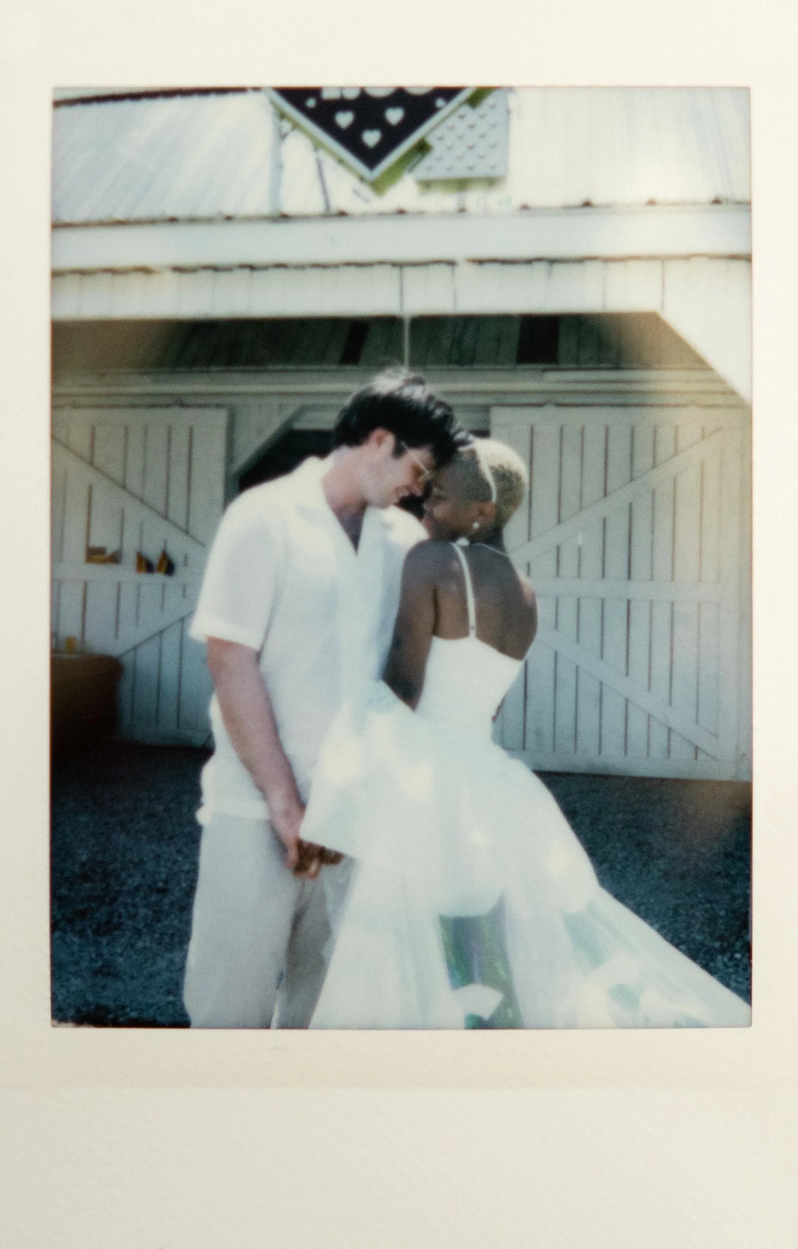 Instant film polaroid elopement photography a bride and groom wear all white and pose touching foreheads in front of the wedding chapel at Bonnaroo. Moody Nashville wedding photography. Documentary Nashville wedding photographer.