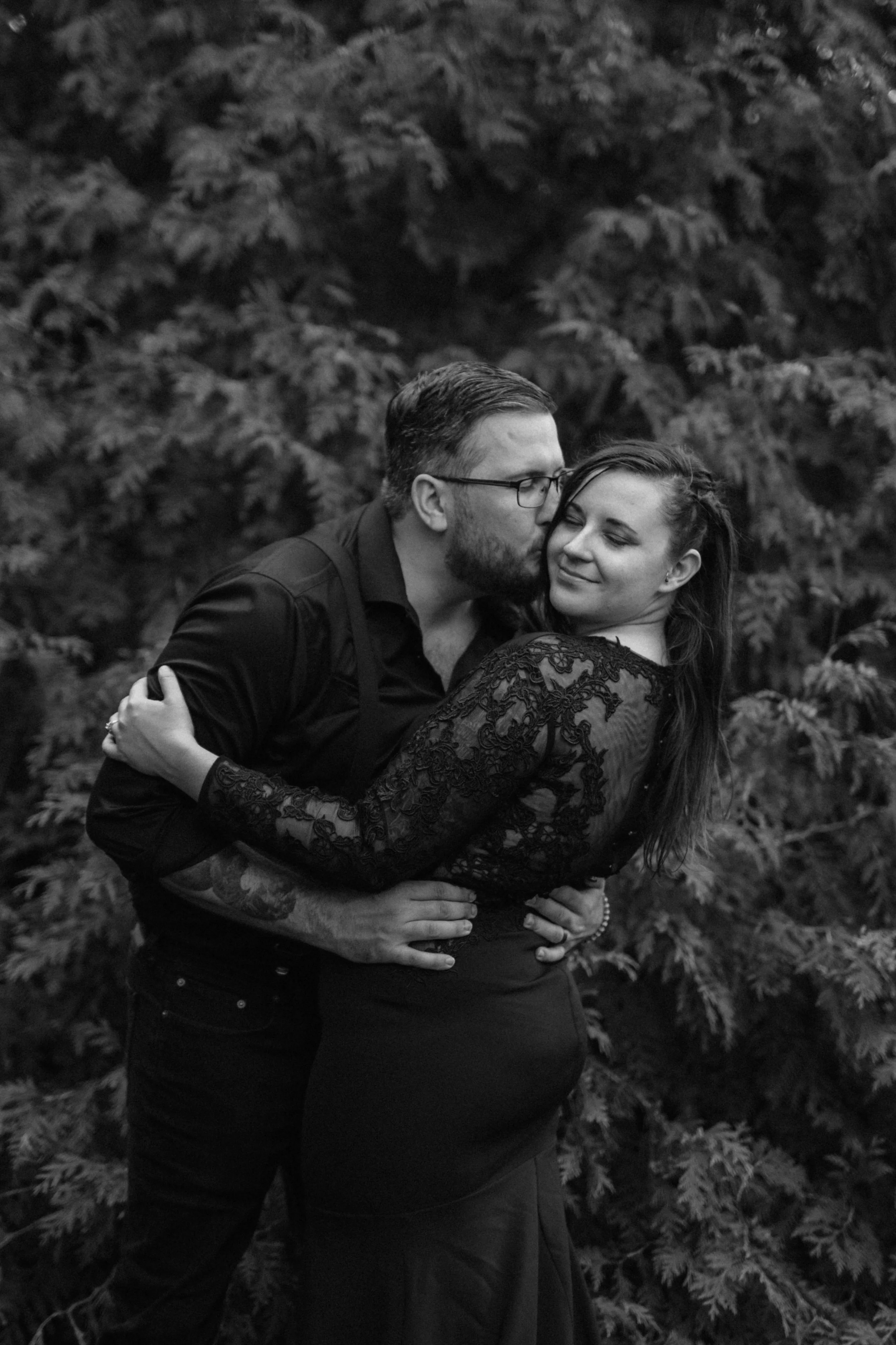 Black and white moody bridal portrait of a groom kissing a bride on the cheek.
