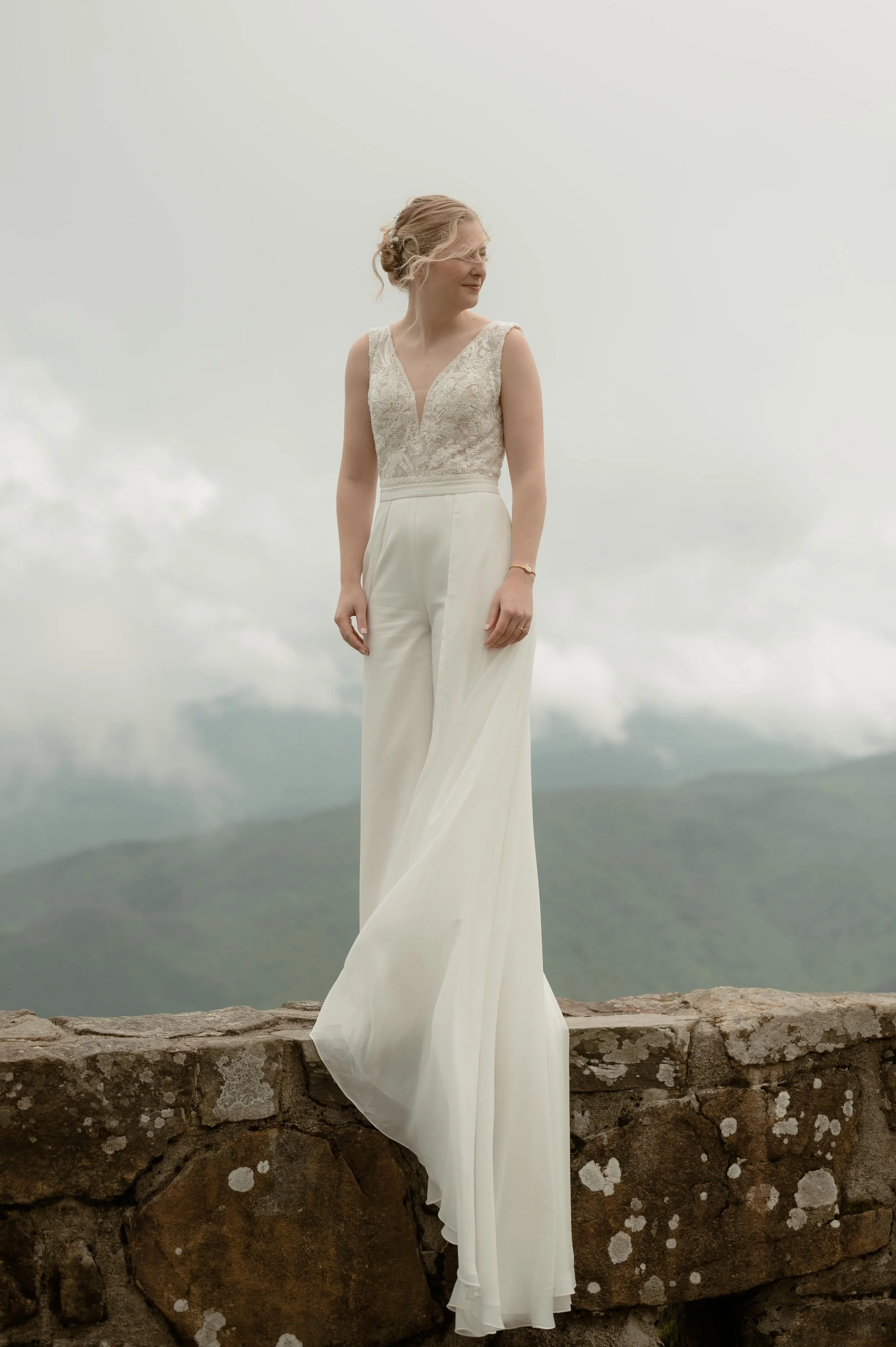 Moody North Carolina wedding photographer a bride poses on a mountaintop overlooking the Appalachian mountains in Nantahala North Carolina. She wears a white jumpsuit with a long skirt attachment. Moody Memphis wedding photographer.