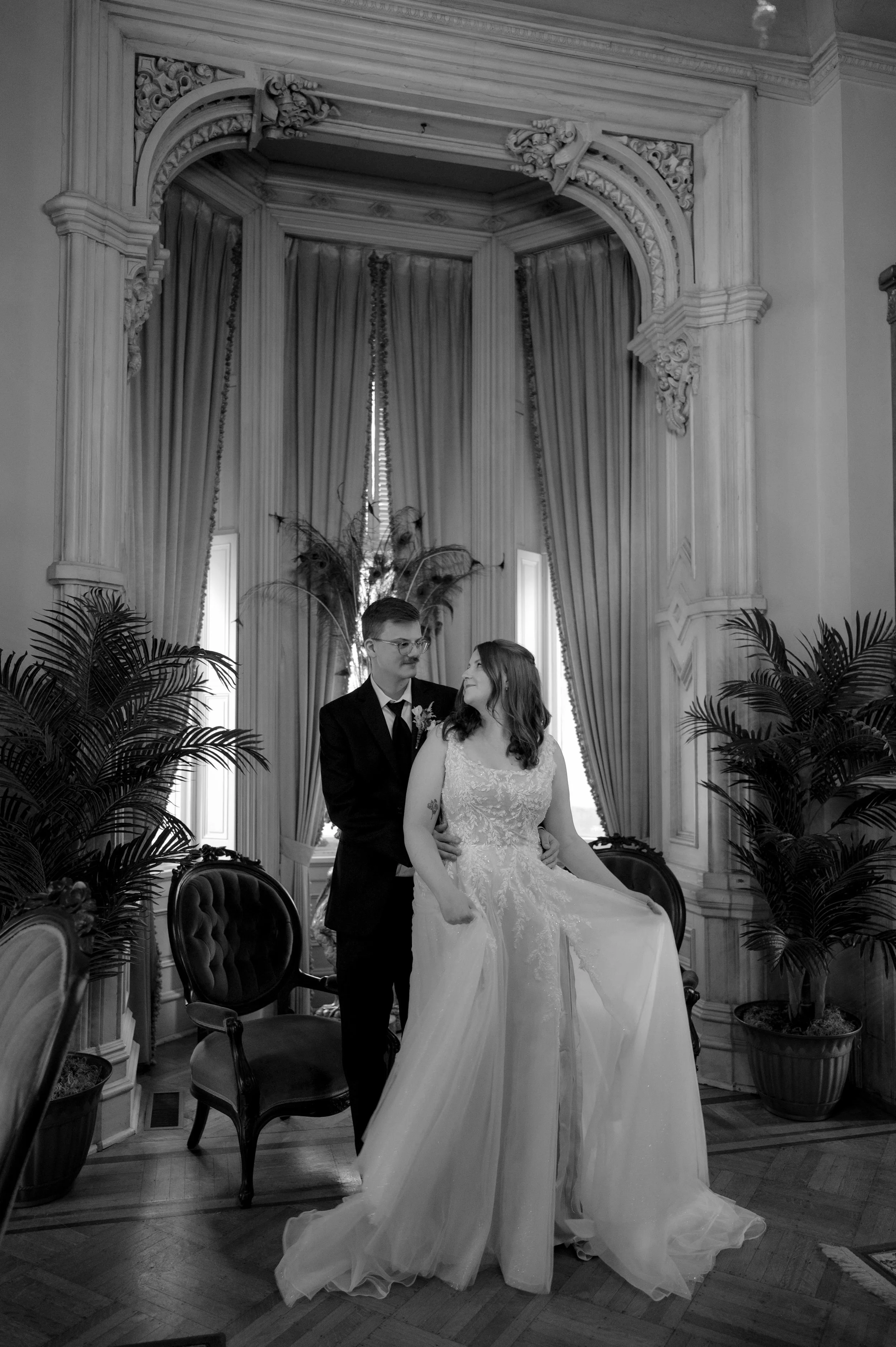 Black and white photo of a bride and groom posing in the Woodruff Fontaine House in Memphis, Tennessee. The bride wears a white wedding dress with a large layered tulle skirt, and the groom stands behind her in a black suit.