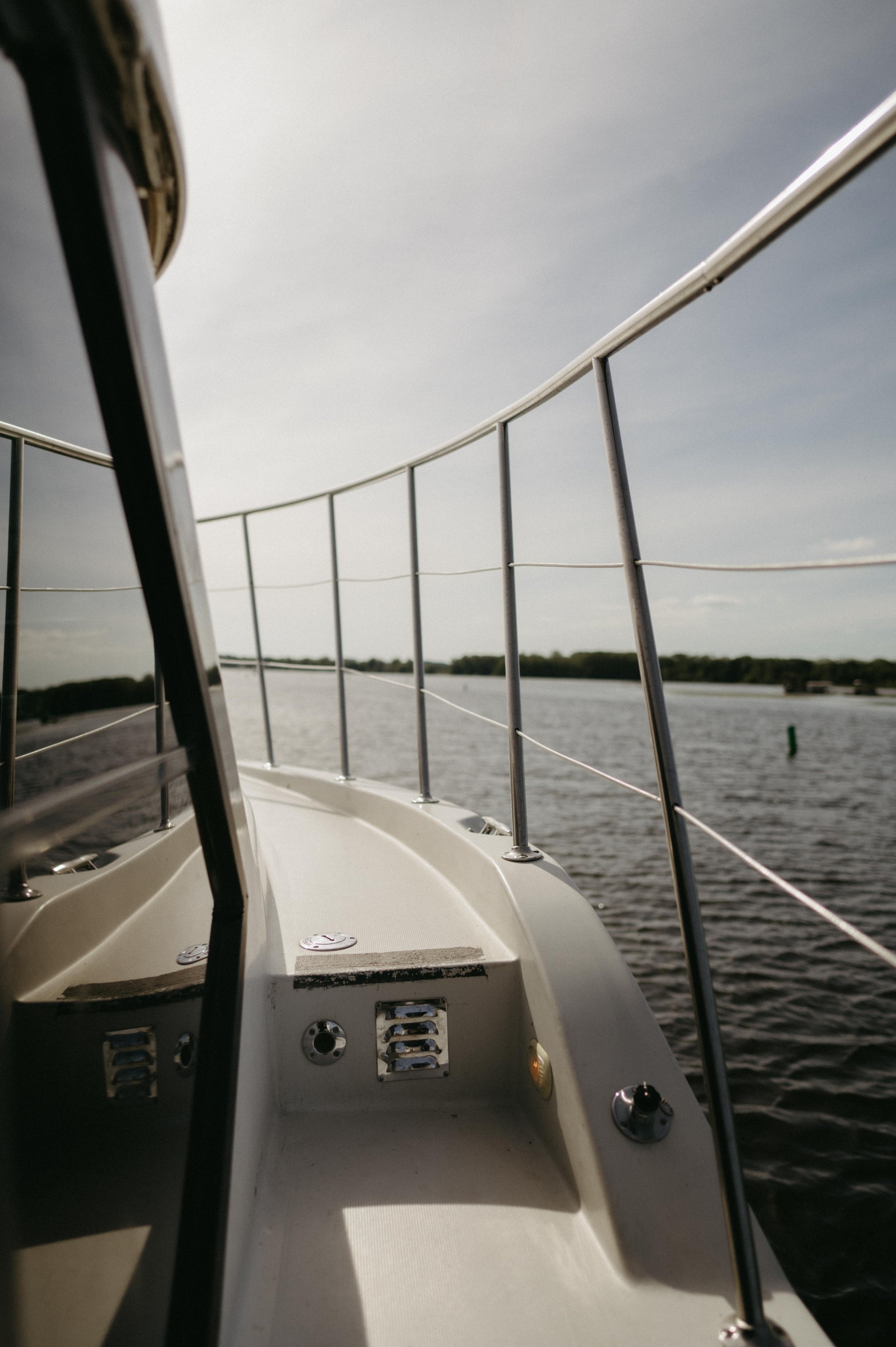 View from the side of the yacht, including the white railing and the front of the boat. The water is a deep grey-blue. Moody Madison wedding photographer. Documentary Madison wedding photographer.