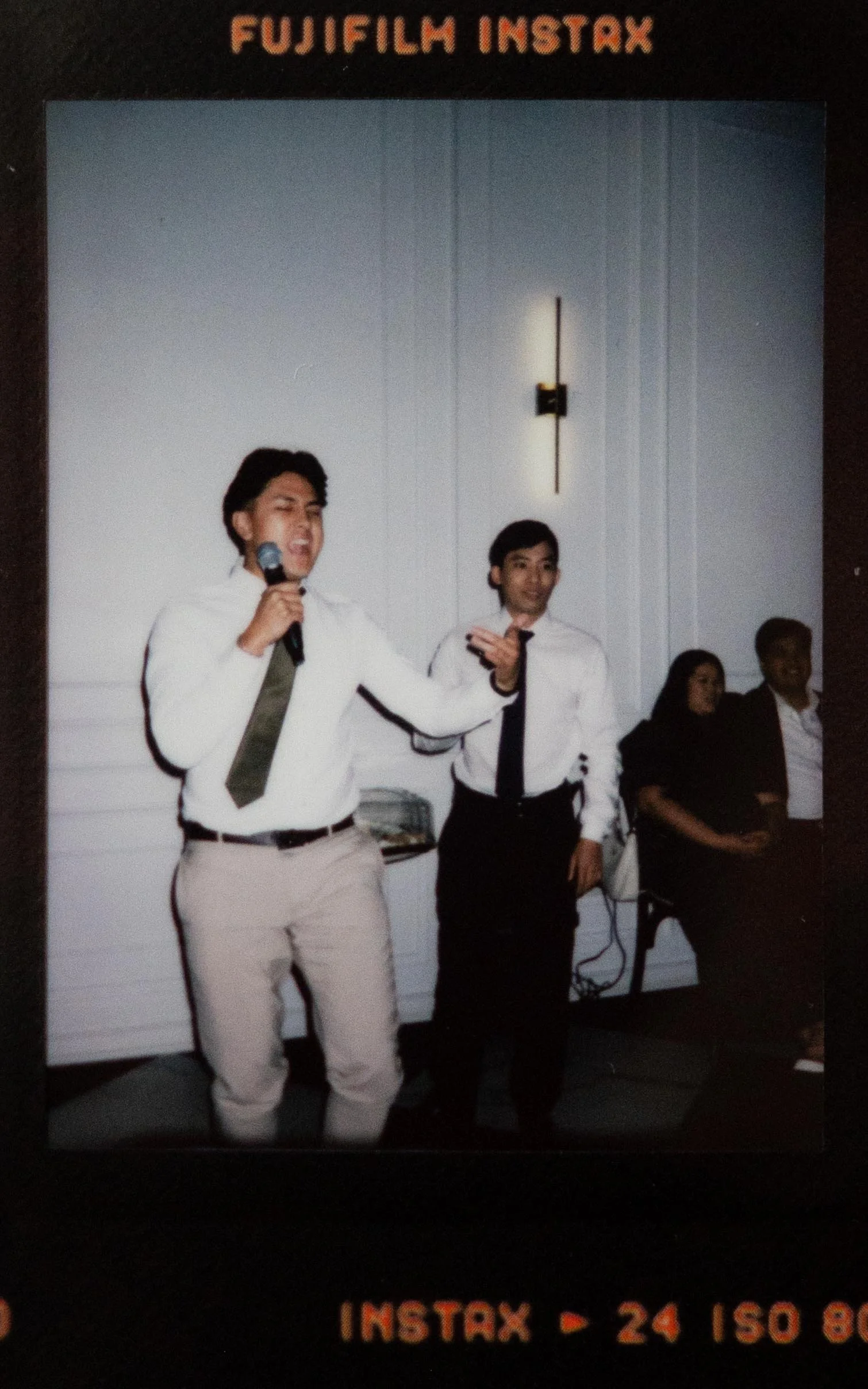 Instant film polaroid wedding photography two guests in white and khaki singing karaoke at a wedding reception in the Parisian in Huntsville, Alabama. Moody Huntsville wedding photographer.