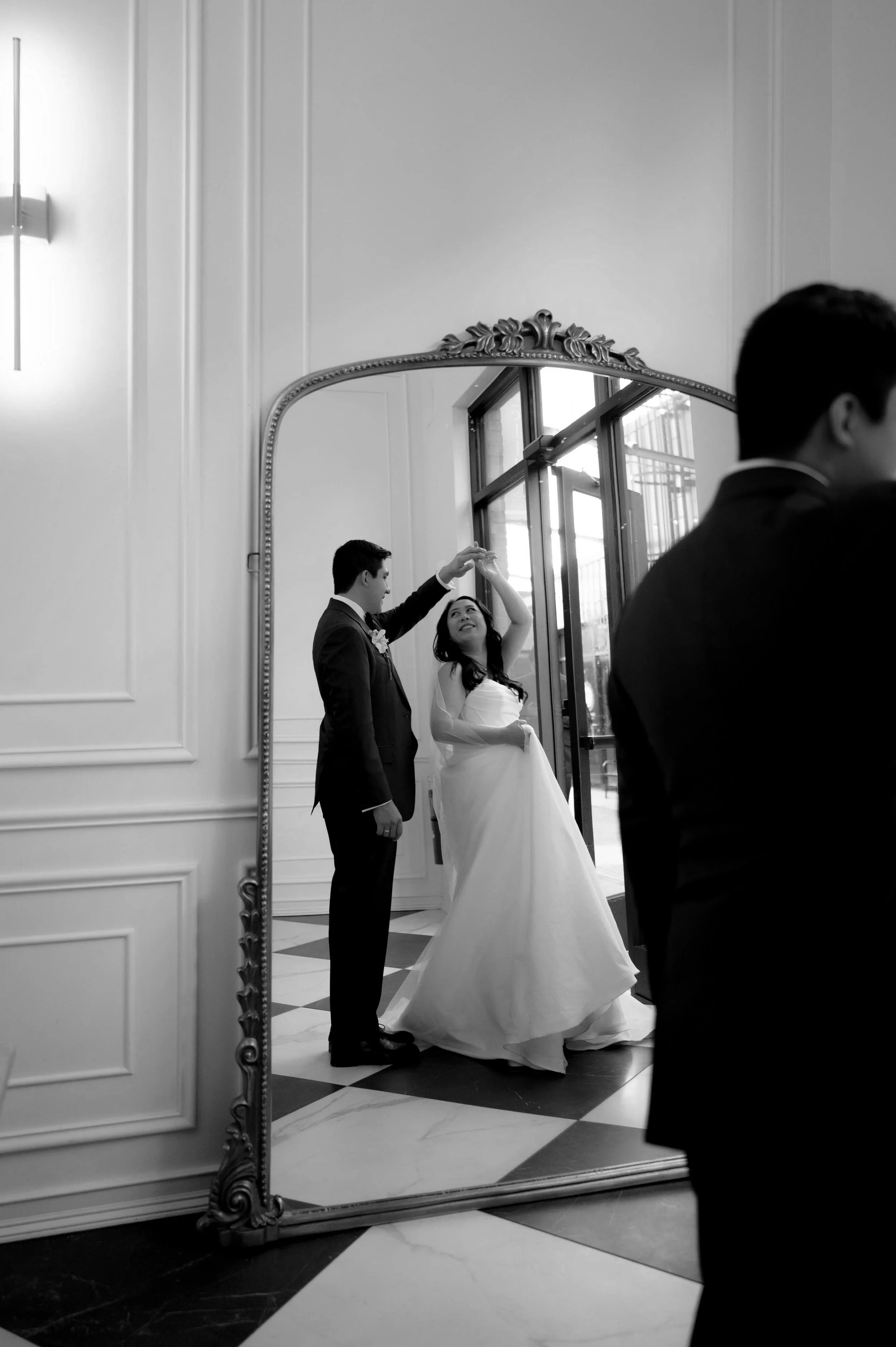A bride and groom dance in front of a large mirror in The Parisian in Huntsville, Alabama. The groom is spinning the bride. The photos is black and white.