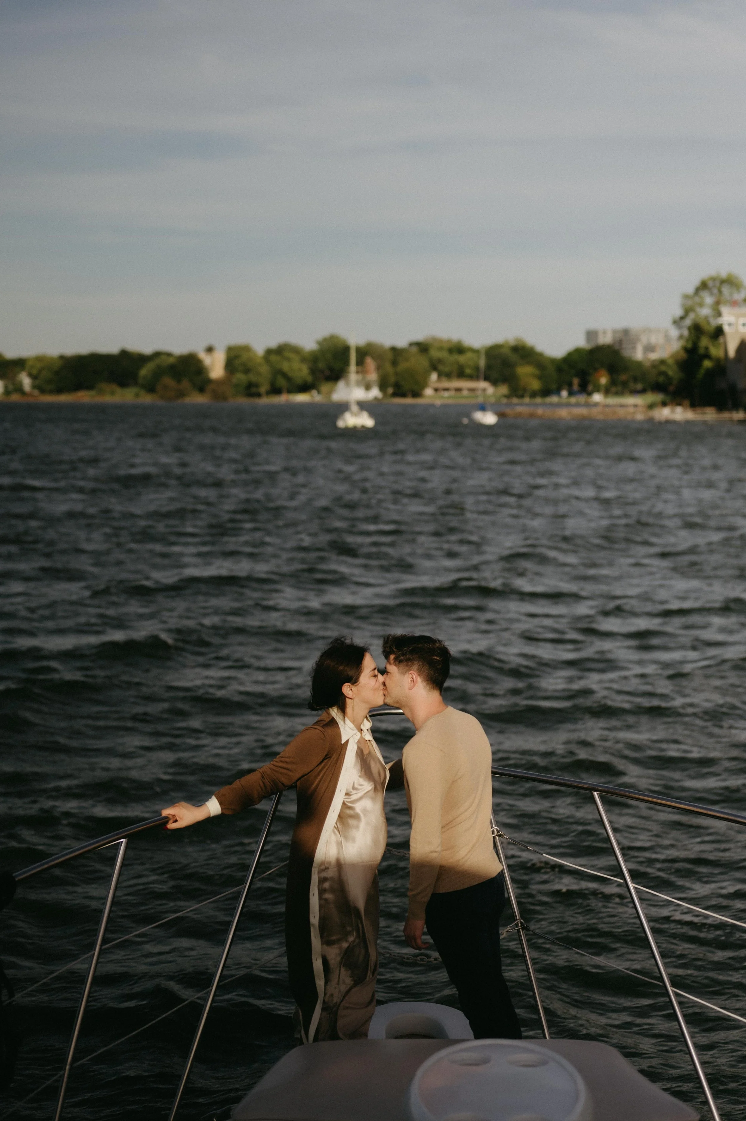 Couple kissing on a yacht with a view of downtown Madison, Wisconsin behind them. Moody Madison wedding photographer. Documentary wedding photographer.