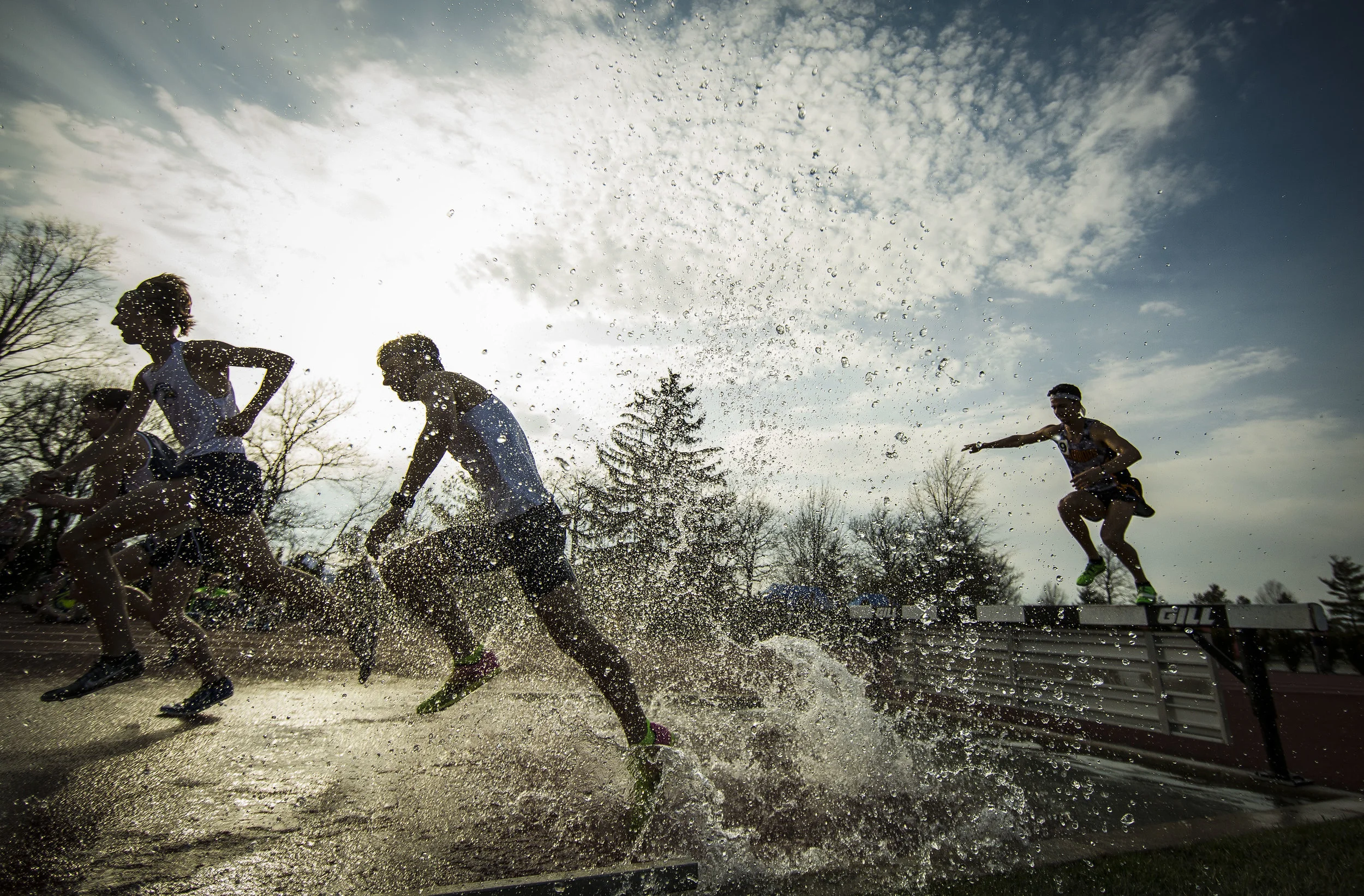 Runners charge through a pool during the 3,000 Meter Men's Steeplechase race, April 13 at Ball State University Track during a 12 school MAC dual track meet. Photos for Ball State Photo Services