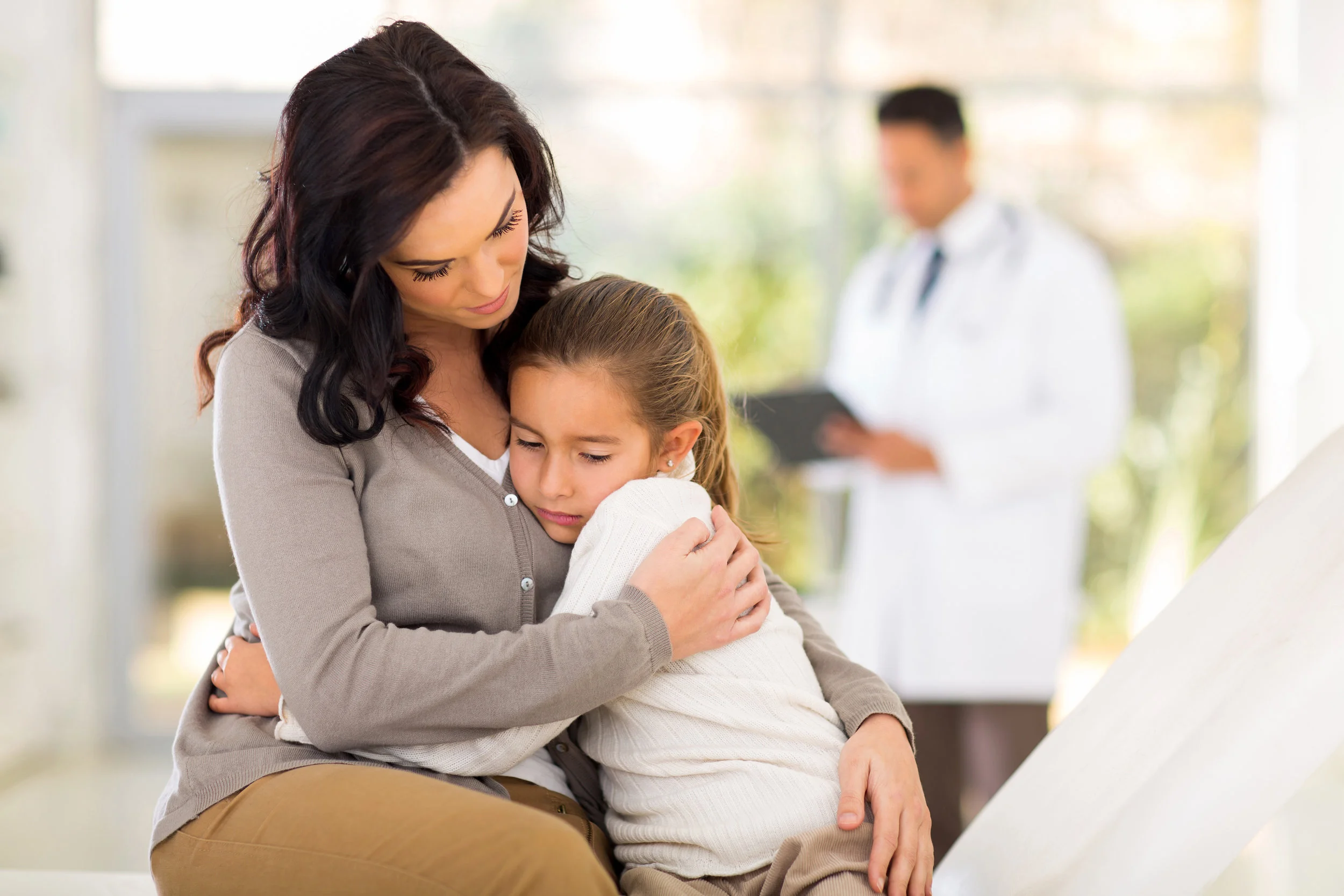 Concerned mother comforting her daughter while waiting for a routine check-up with a family docto