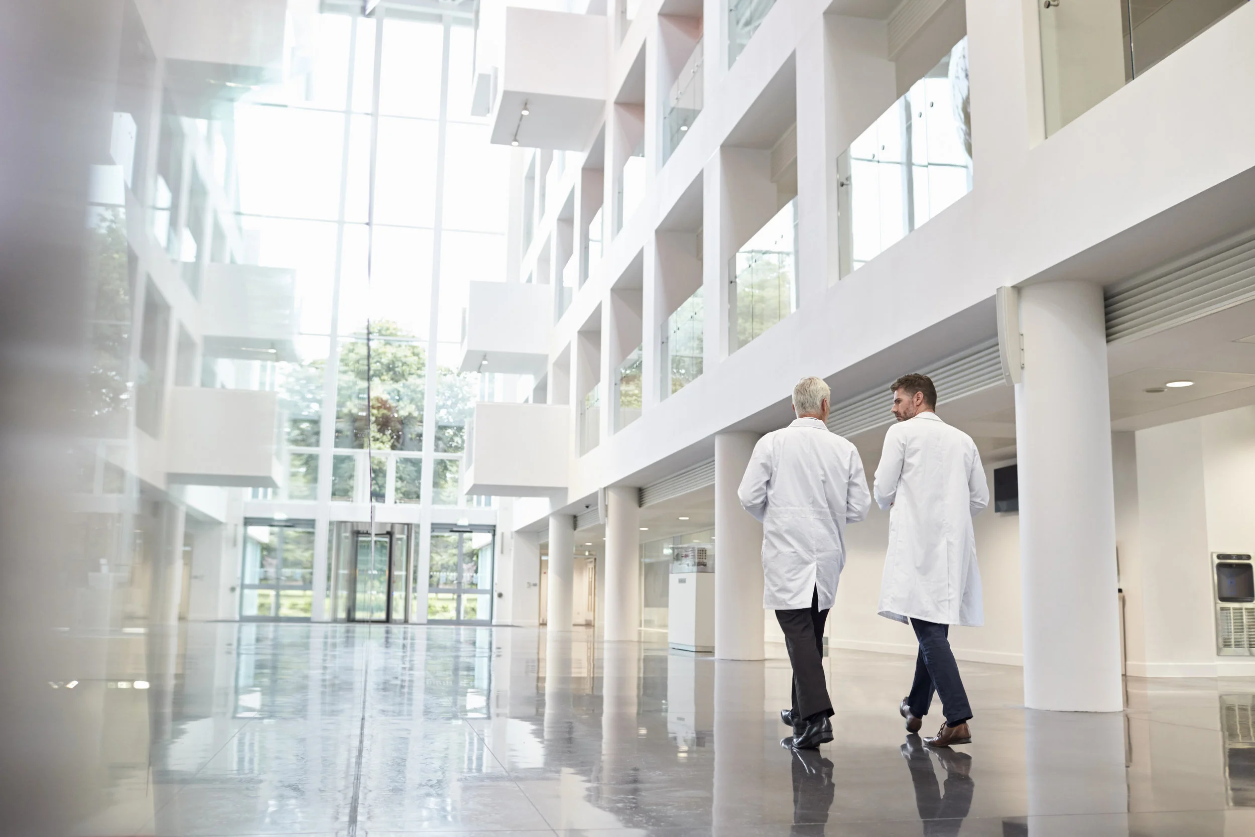 Two male family practice doctors in white medical coats walking through the lobby of a hospital or healthcare facility