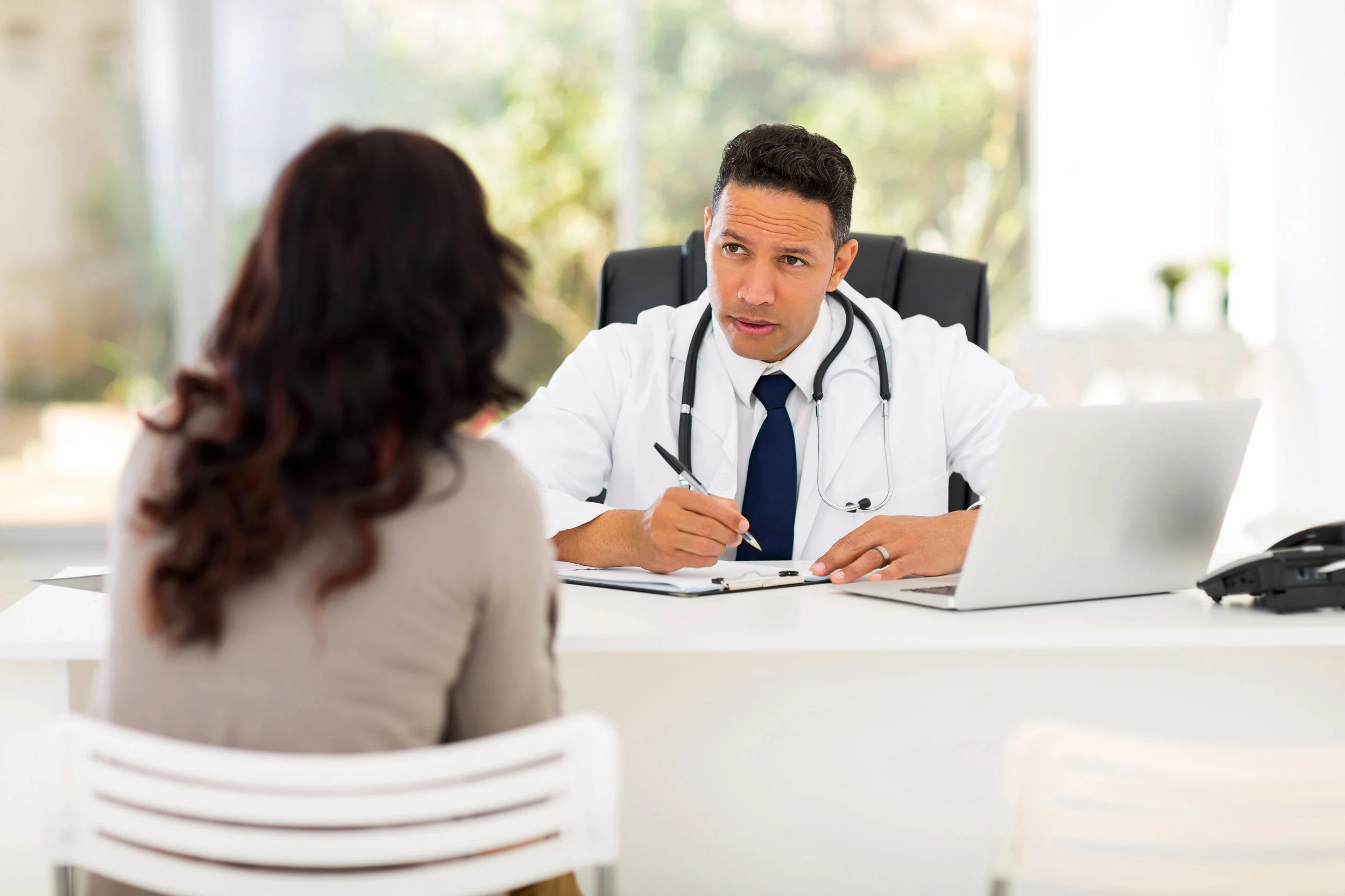 Professional medical doctor consulting with female patient in office, encouraging physician patient interaction