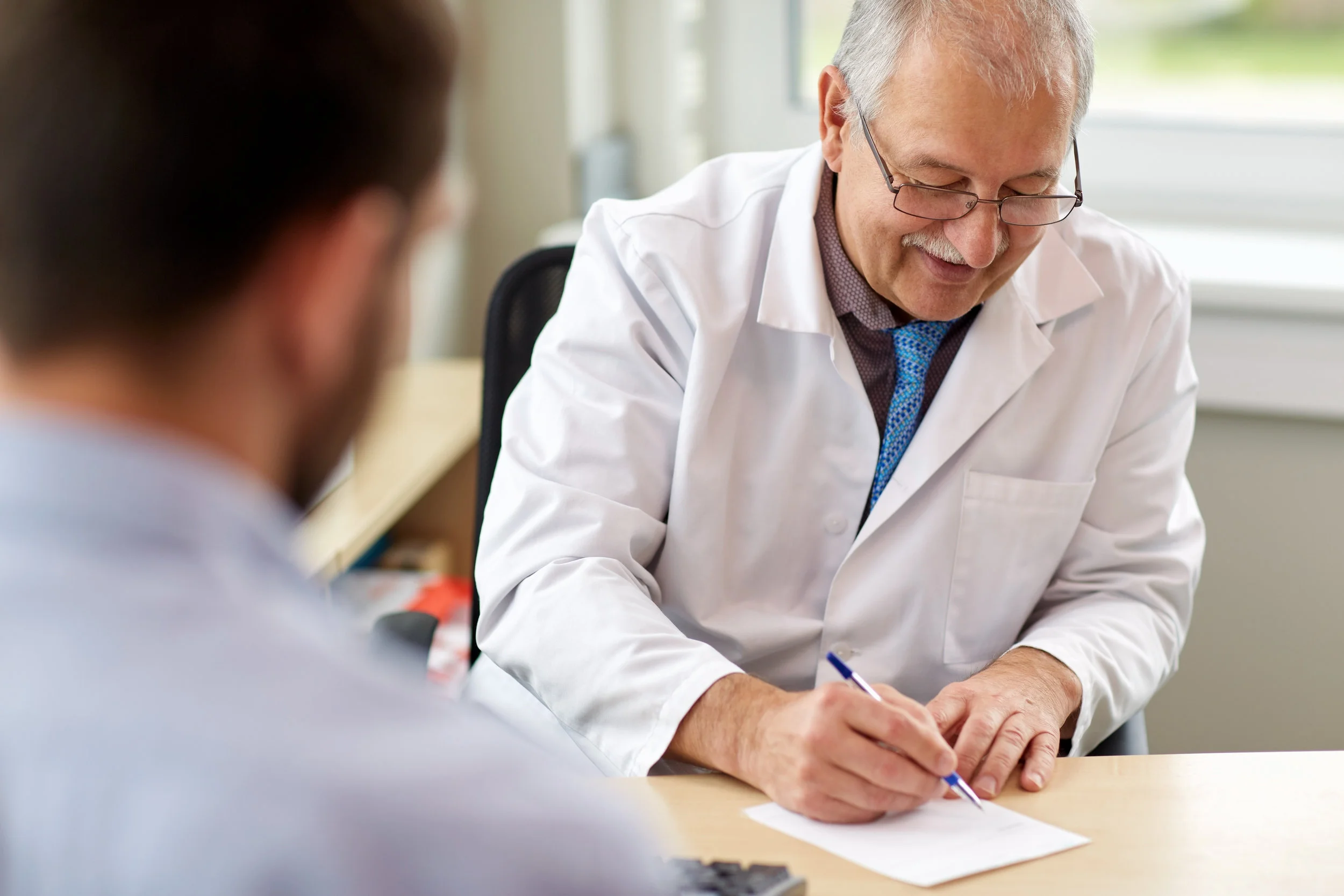 Older male doctor writing a prescription for male patient at a clinic