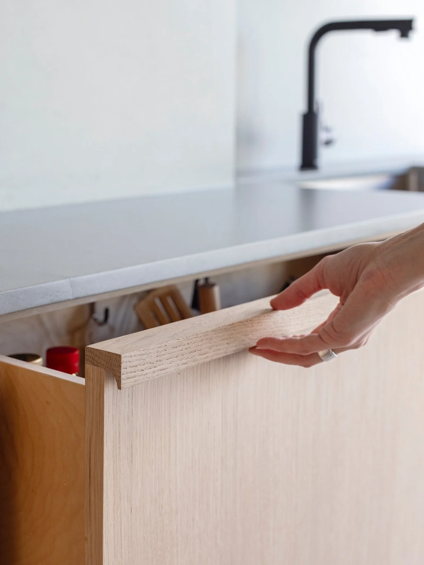 This solid white oak integrated hardware turned out wildly beautiful. 
Not only does it integrate into the door fronts, but it also integrates into the overall kitchen design. It flawlessly disguises itself as part of a gable in the grid-like patter