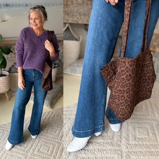 women stadning in jeans white boots purple knit jumper brown handbag.