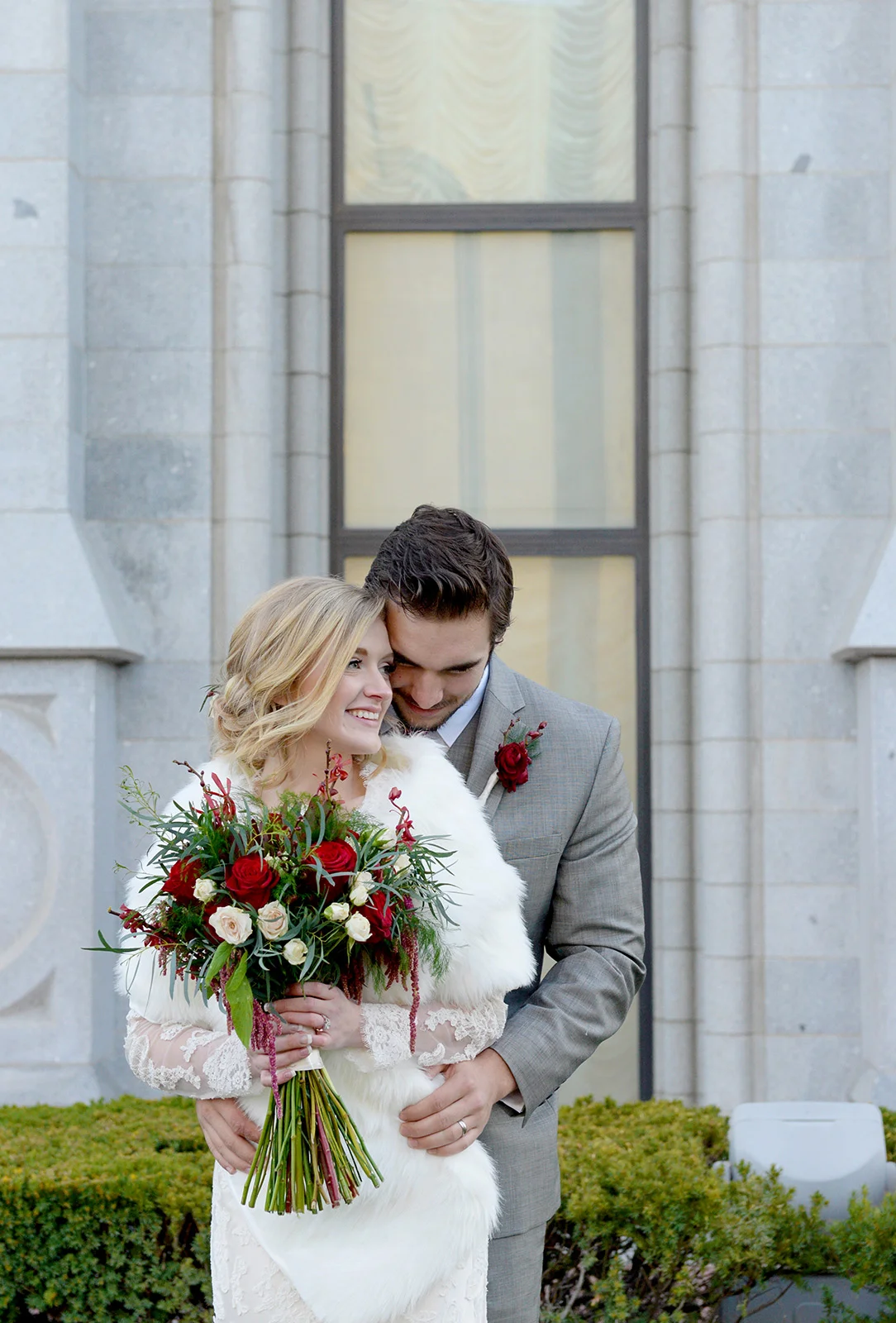 A groom holds a bride with her fur wrap and bridal bouquet in front of a church.