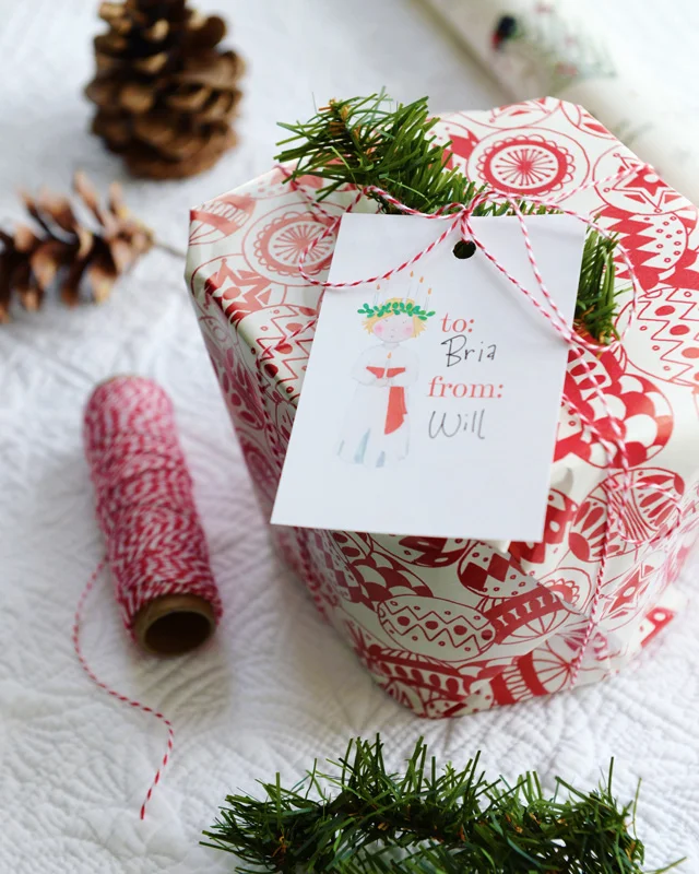 Printable gift tag sheet features St. Lucia girl with candle crown and white robe with red sash, and "to" and "from." Prints nine tags per 8.5x11 inch sheet.