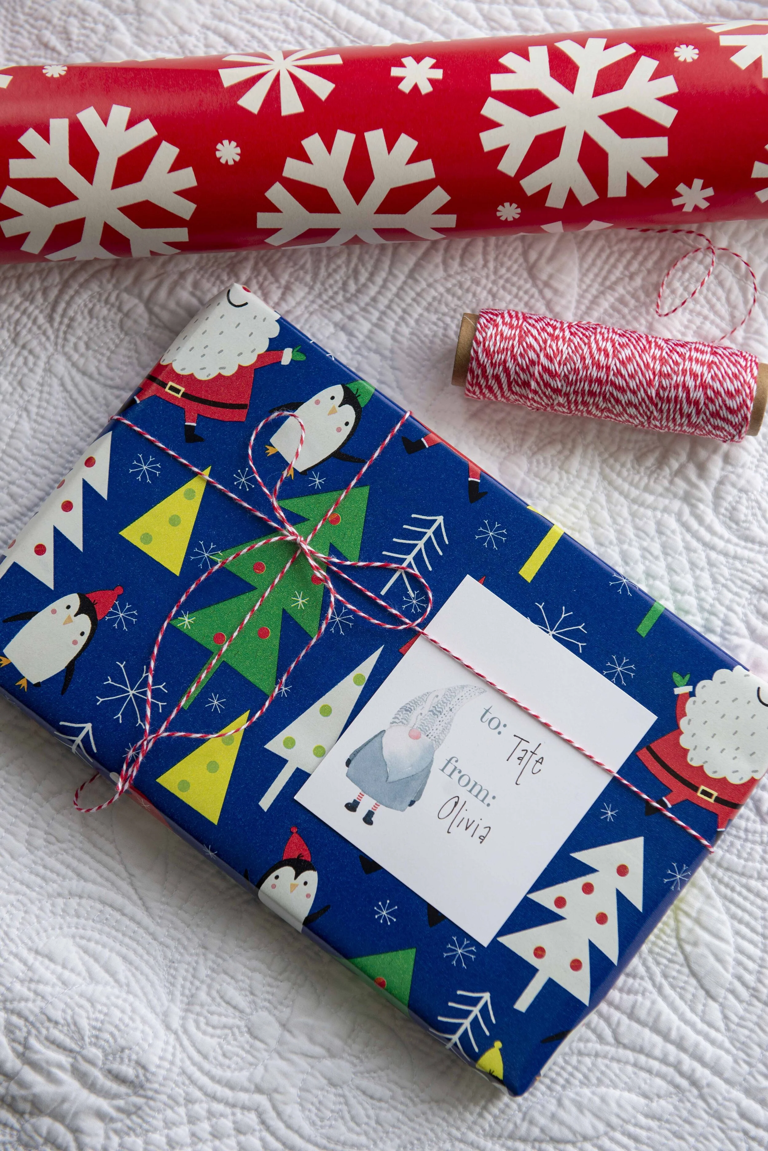 Gray watercolored gnome gift tag tied onto a Christmas gift bag with black and white twine and sprig of pine. PDF download of tags available here.