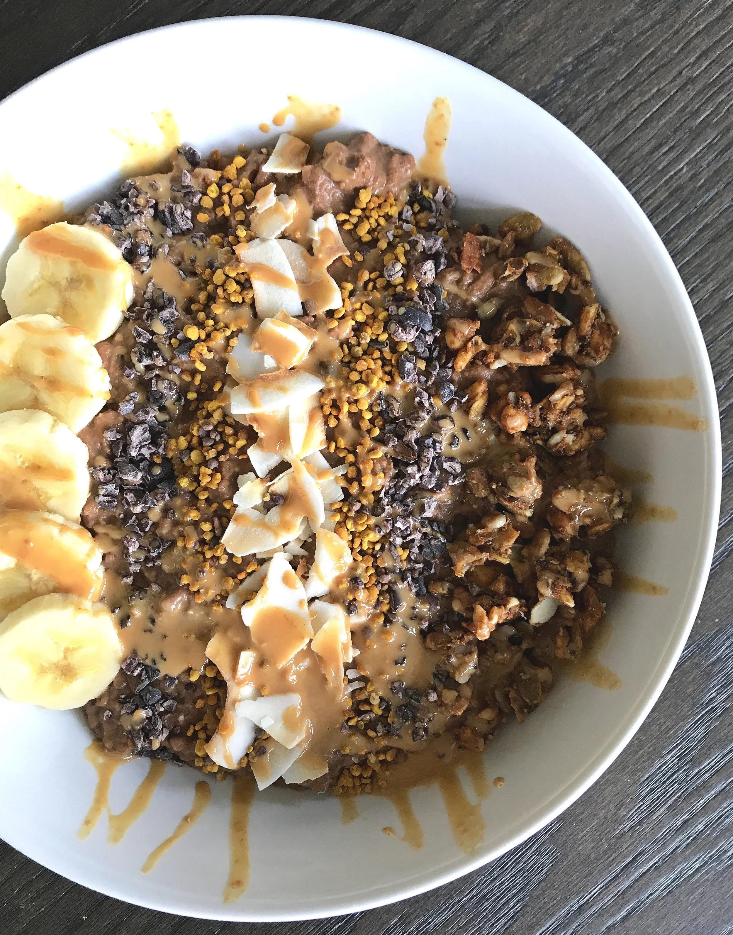 Chocolate Sweet Potato “Noats” topped with sliced banana, cacao nibs, coconut flakes, bee pollen, grain-free granola, and a drizzle of warm cashew butter.