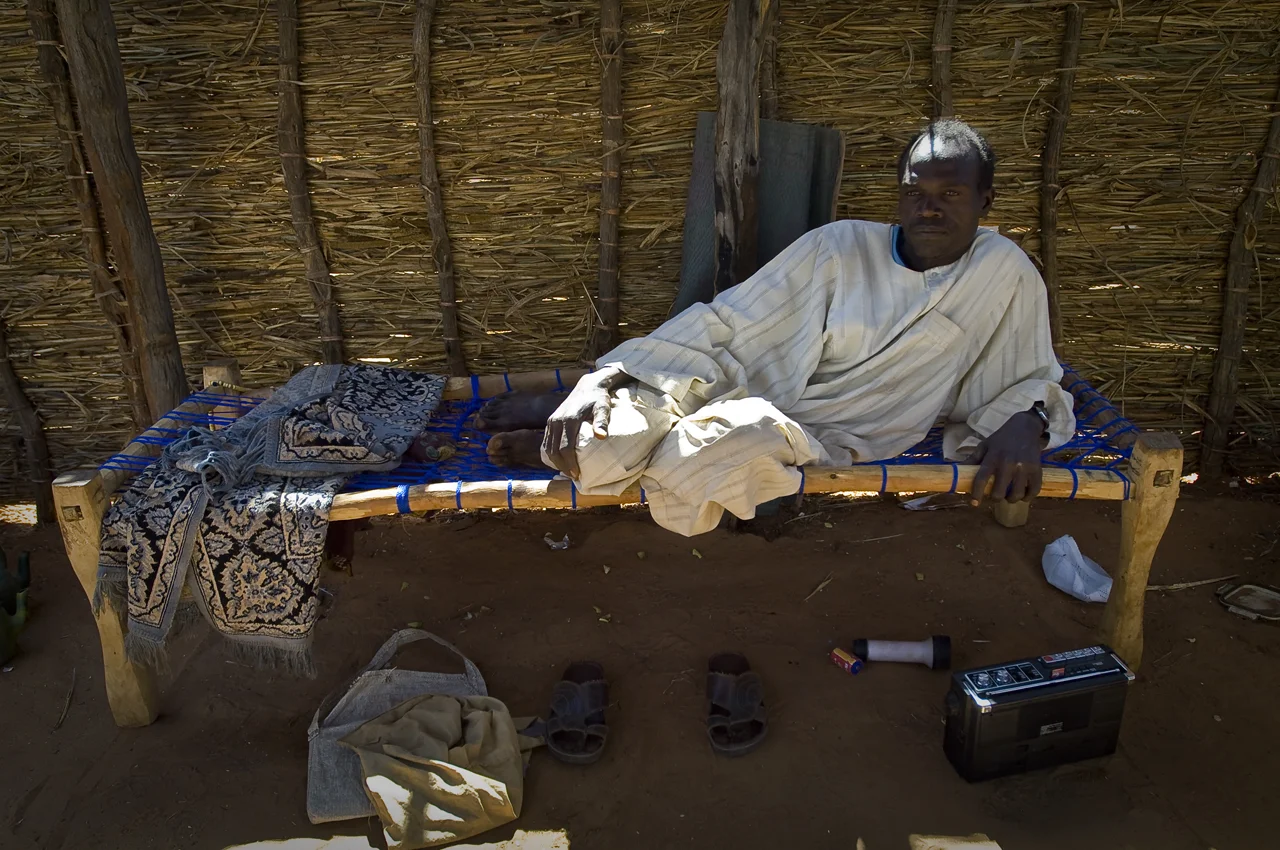 In the courtyard of the family's compound, a refugee is resting, listening to the radio. It is market day in Goz Beida, the big chadian city located 4 kilometers away from the camp of Djabal which sheltered 17.766 persons and 4.681 families in december 2011. Many people went there. The camp is day sleeping.
