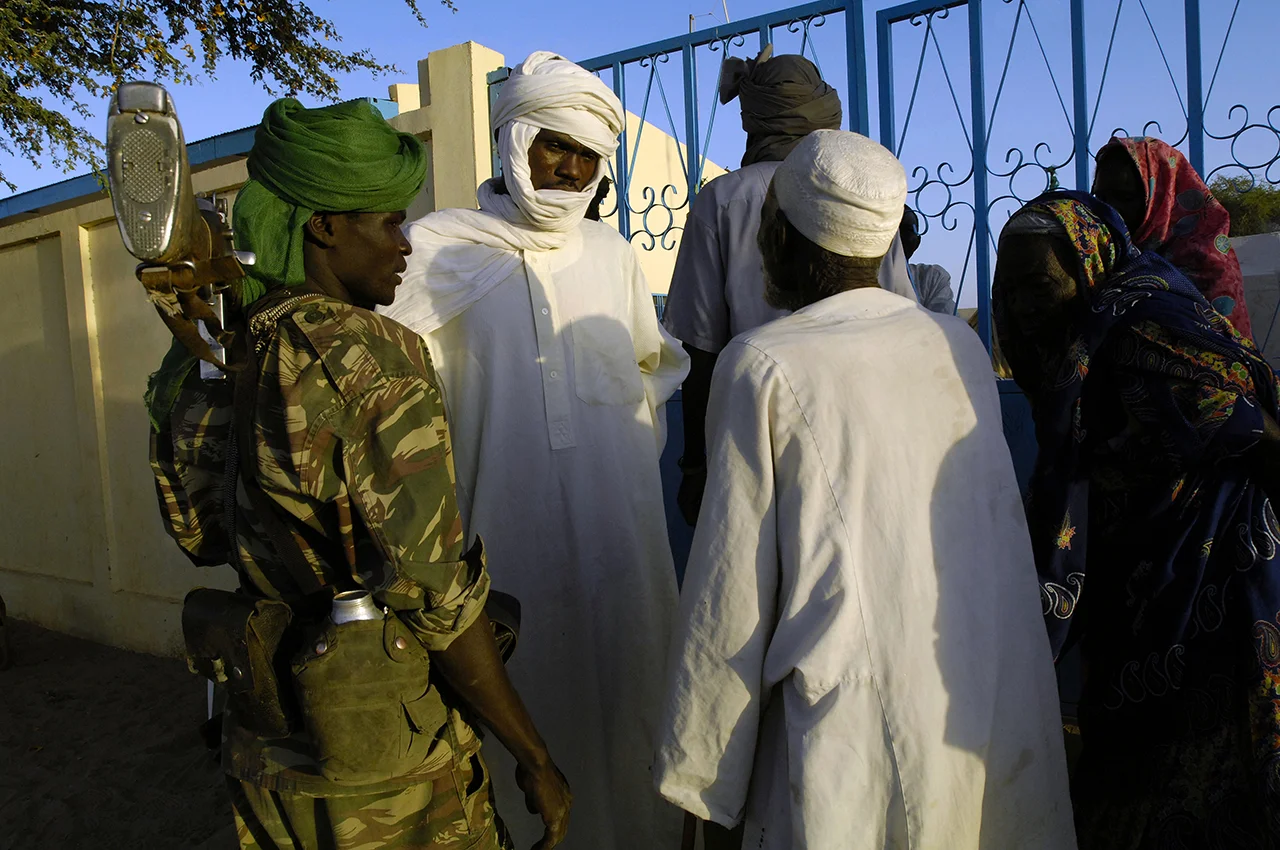 Traditionnal leaders talking with chadian and refugees, while a fighter, refugee himself, in charge of refugees security looks upon.