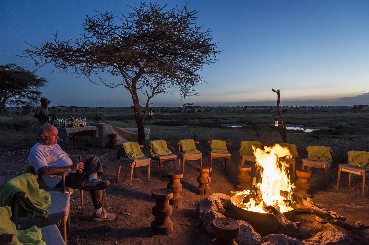 A tourist enjoys beer, next to a campfire at Asilia Camp, the only tent camp located in the eastern prairies of the central part of the Serengeti, magnet for cheetahs and lion, out of the frequent passing paths of tourists , because out of the way. The permanent camp of 8 luxury tents is set up more than an hour from its nearest neighbor. Approximately 2,700 beds in approximately 120 safari camps are available throughout the park.