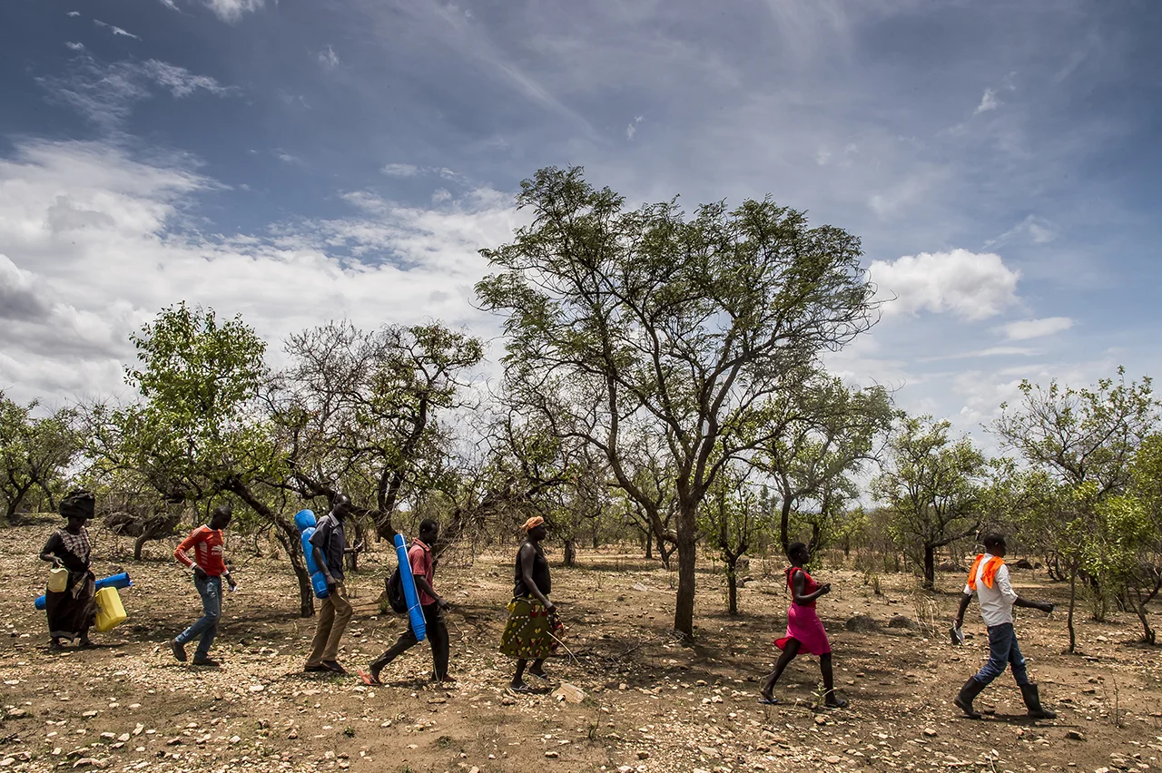 Bidibidi settlement area. An official of the Office of the Prime Minister (OPM) leads the heads of refugee families to the plot of land allocated to them in a wooded and stony area.
