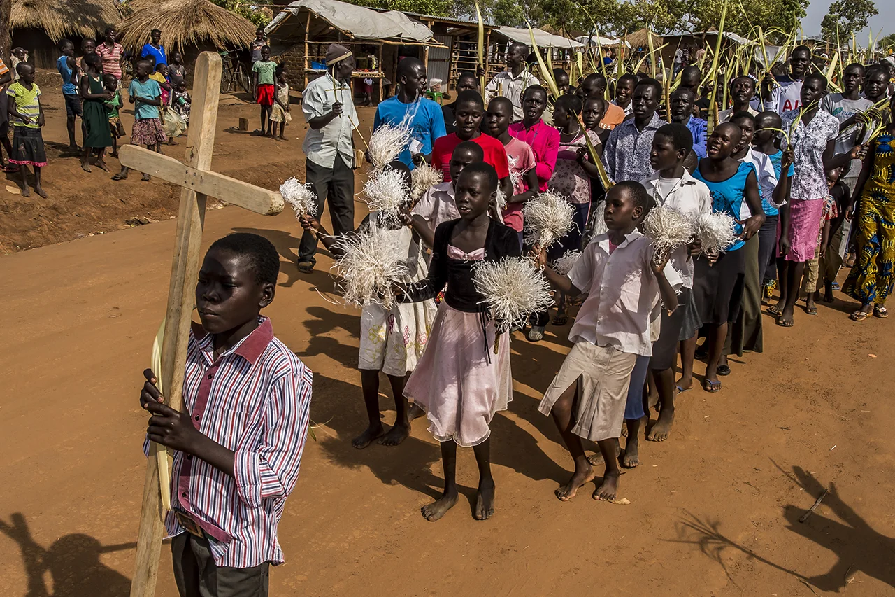 On Palm Sunday, a procession walks through some areas of the Bidibidi settlement area. It will end under a large tent that serves as a church to the many South Sudanese Catholics, durant a service with the delicate sound of traditional harps.