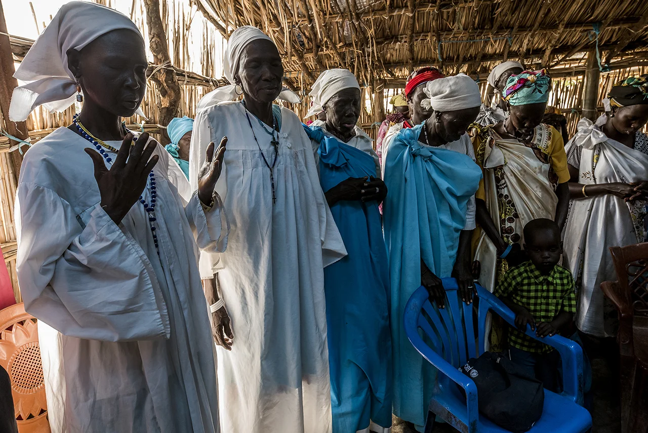 Community elders praying during Sunday morning service in the Old Fangak Presbyterian Church, a large hut with a reed roof dislocated on its ridge. The Presbyterian Church is the main religious organization in the Nuer regions.