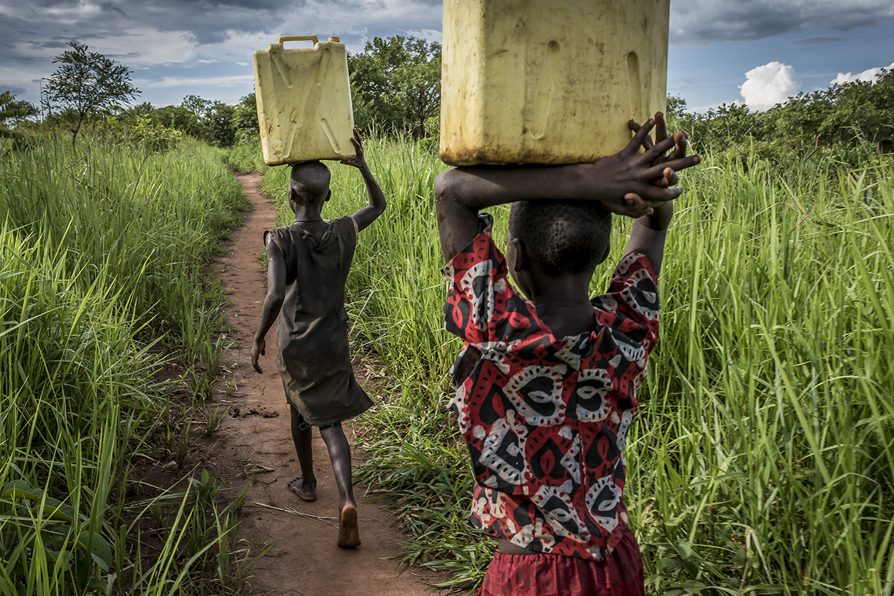 Nearby the village of Coo-Rom, two young girls, relatives of Dominic Dominic Ongwen’s nieces carry back to the family compound jerricans of water, collected in a nearby water pump. Dominic Ongwen's relatives lived in 2 nearby and different homestea