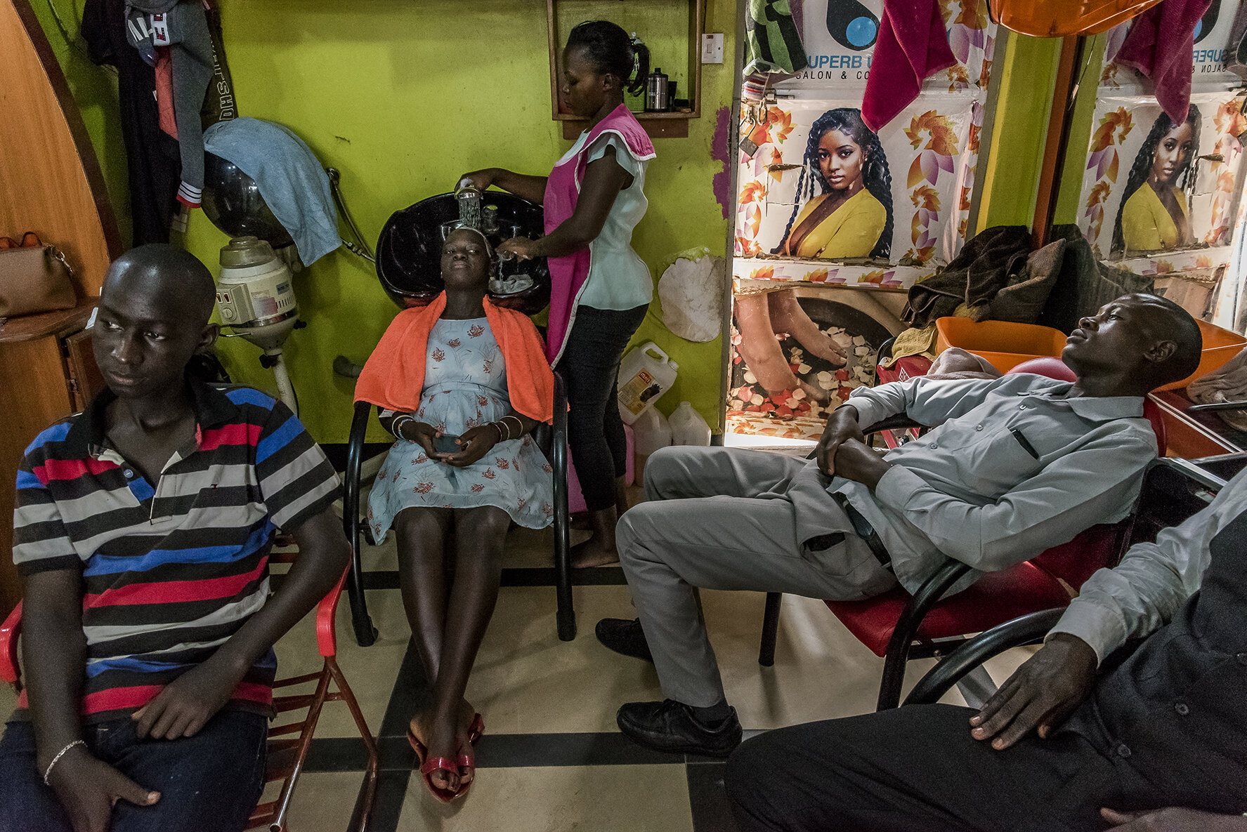 In the Super B hair salon, in the area of the hotel where the contestants will spend the last night before the competition, a hairdresser is doing a shampoo for a candidate while some males candidates are waiting for their turn.