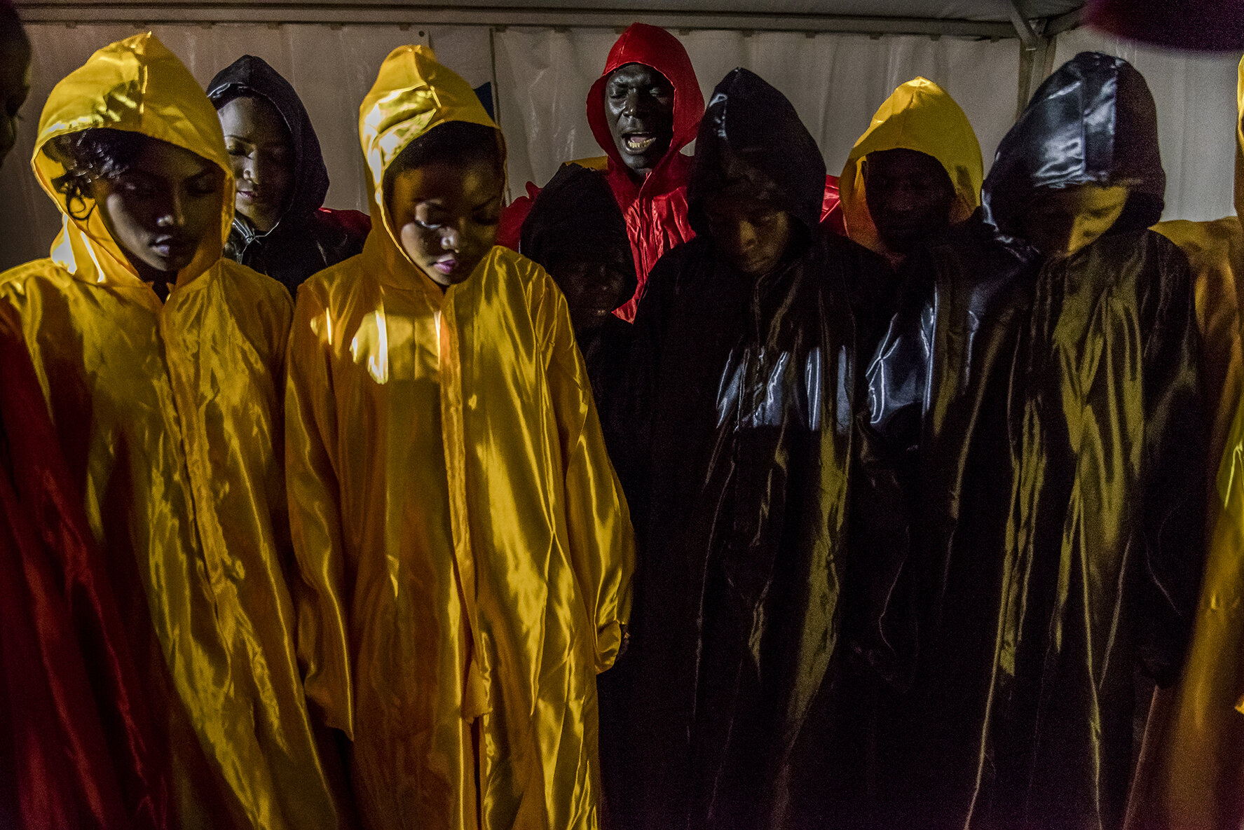 One of the nine male contestants of the beauty pageant is a pastor. Backstage, before the opening choreography executed by the sixteen contestants, wearing ponchos in the colors of the Uganda flag (Yellow, black and red), he leads a prayer (in red)