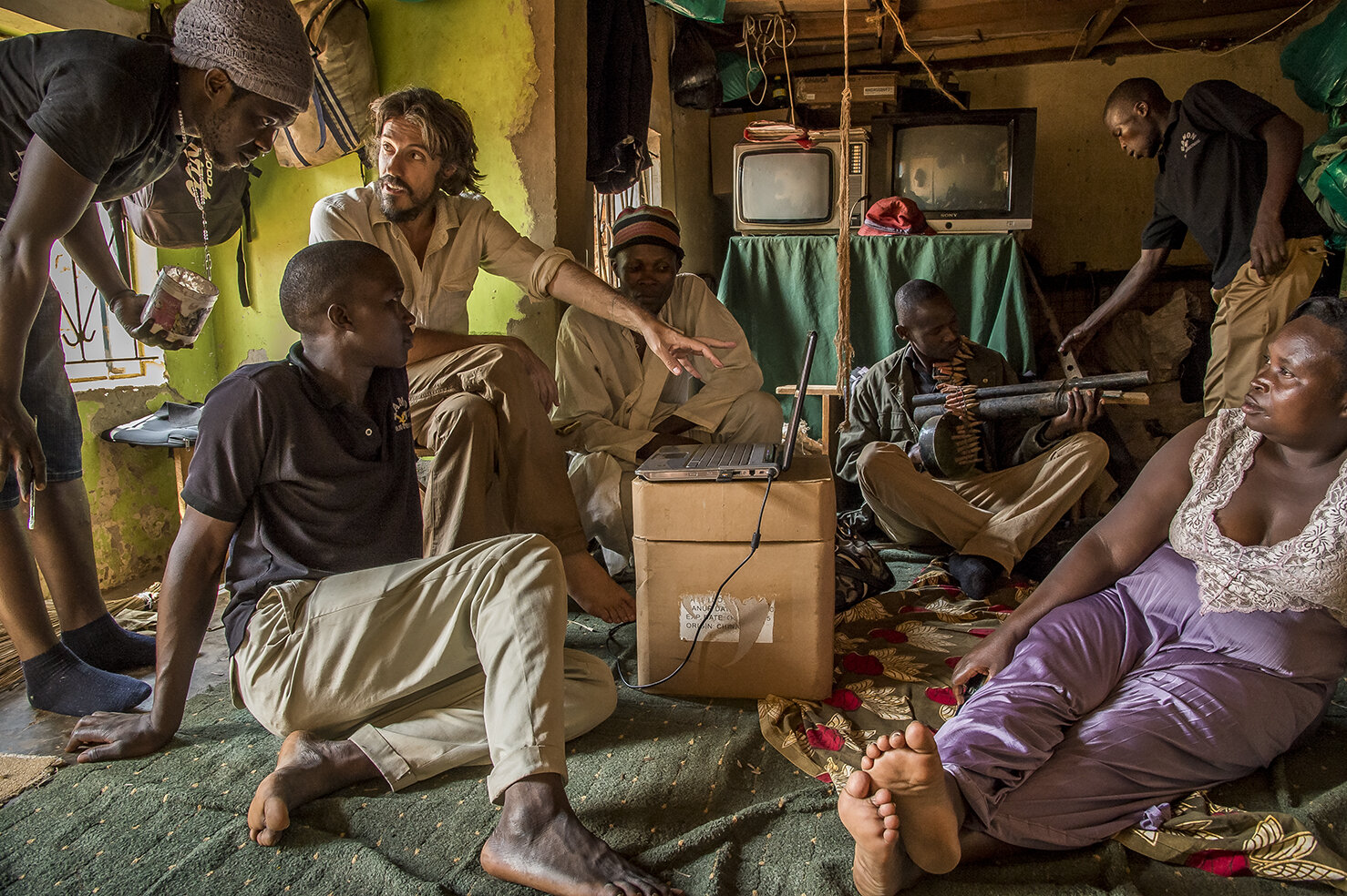  Alan Hofmanis shows to Henry Kato Magumba, « The Barbarian » (left), actor, stuntman and graphic designer, a logo that he wants him to draw on a poster, in order to put it on social media, for the promotion of Wakaliwood. Around them, some comedians