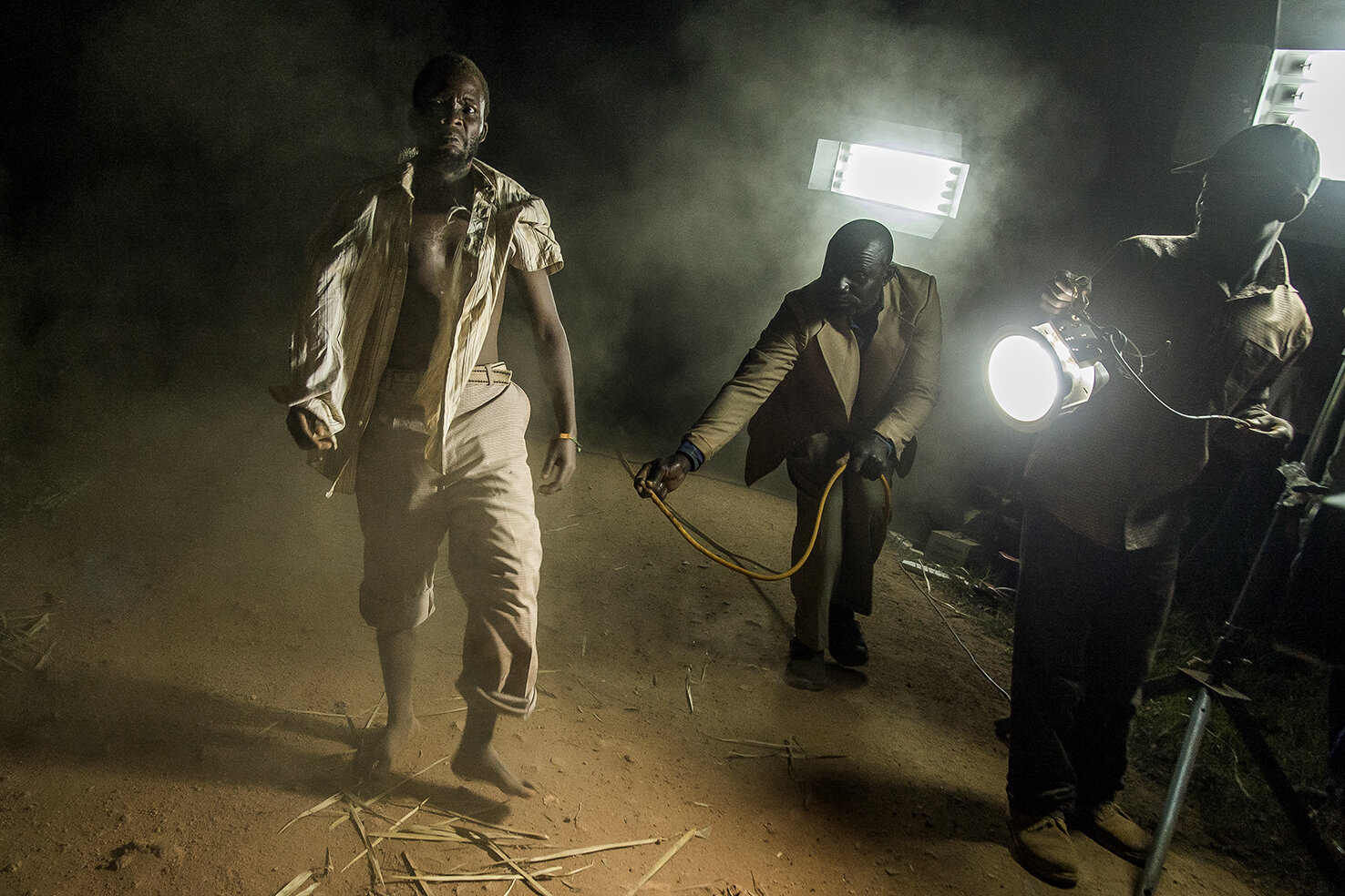  In Kaliti village, 30 kms away from Kampala, an actor plays the part of a zombie walking in the night on a road. Behind him, Daouda, the props man creates a dust cloud with an air compressor, while a comedian lights up the scene. In the bush, Ramon 