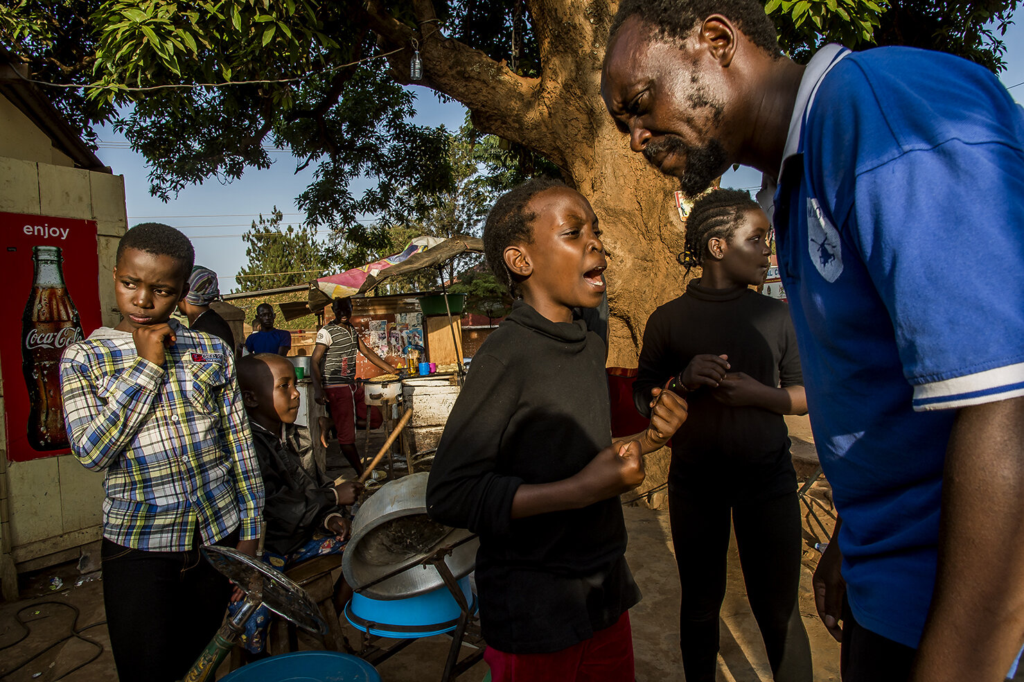  In a street of a remote area of Kampala, during the shooting of a scene of a musical, coproduction between Wakaliwood and a musical producer, Isaac Nabwana listen to his daughter, Racheal M. Natembo, main character, rehearsing her song. 