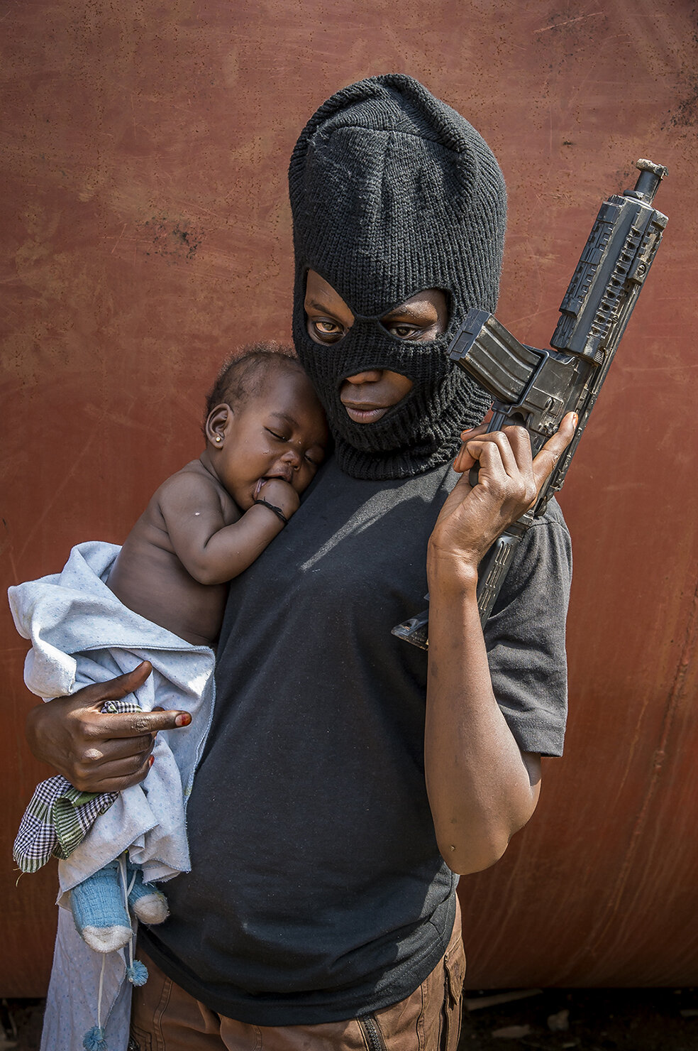  Brenda Nantume, hairdresser to make a living, in hoodlum’s outfit, holds her daughter. She covers about 30 kms to be part of the shooting. 