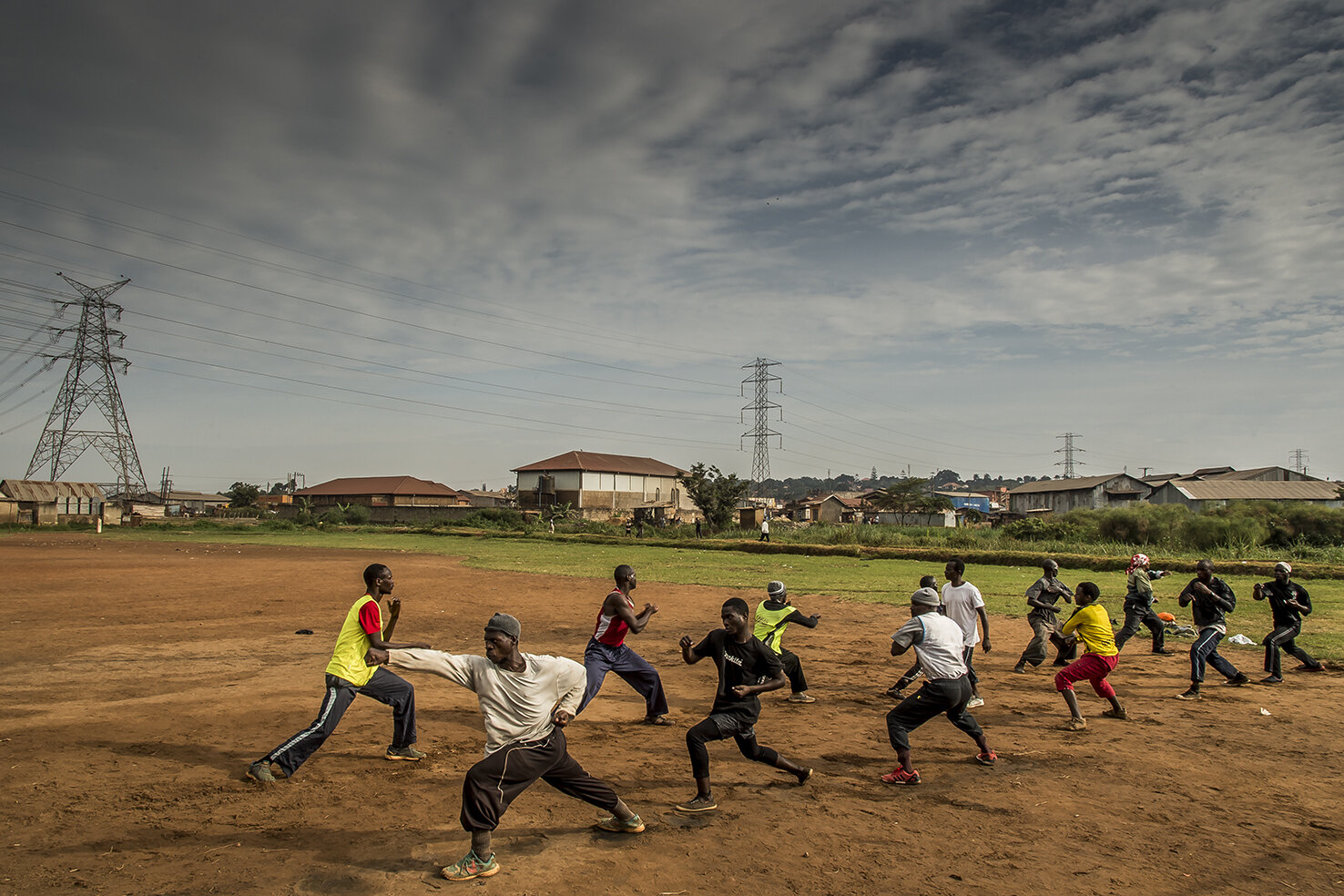  Half-brother of Isaac Nabwana, the director/producer of Wakaliwood, Robert Kizito (white teeshirt walking between the ranks) gives his Kung Fu class every Sunday on a football pitch in the out of the way area of Natete. Amongst the assistance, three
