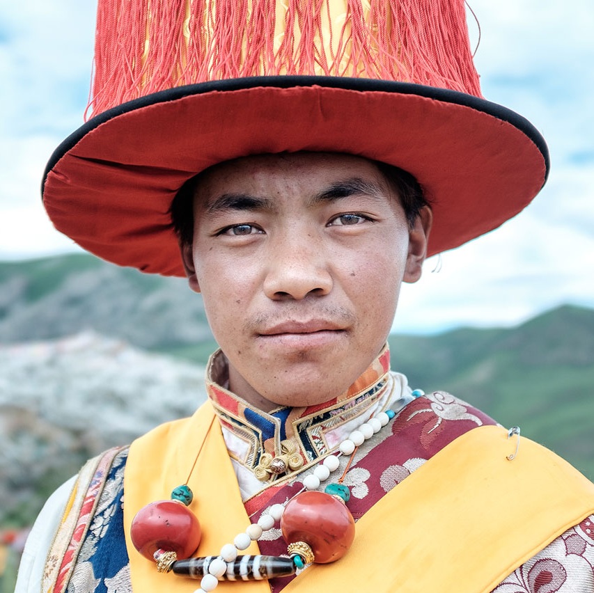 Young Tibetan man in traditional ceremonial dress and red hat, portrait photography from Yushu, China — Oliver Maximilian, KULTURHYBRID®