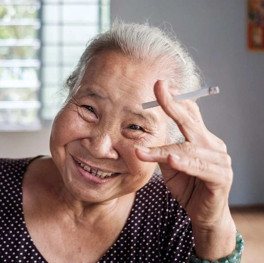 Elderly Vietnamese woman smiling and holding a cigarette, close-up portrait — documentary travel photography from Vietnam by Oliver Maximilian, KULTURHYBRID®