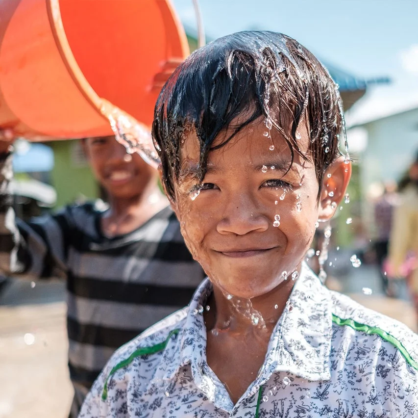 Young Cambodian boy laughing as water is poured over his head — candid street portrait from Cambodia by Oliver Maximilian, KULTURHYBRID®