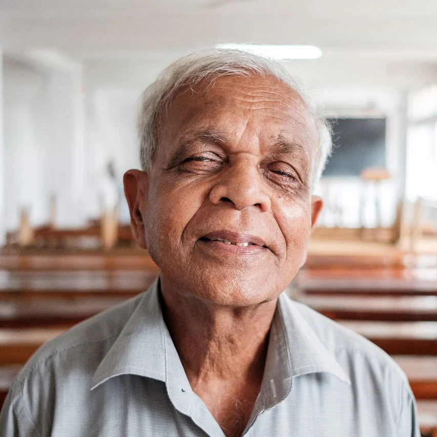 Elderly Sri Lankan man with grey hair, soft expression, seated indoors — intimate documentary portrait from Sri Lanka by Oliver Maximilian, KULTURHYBRID®