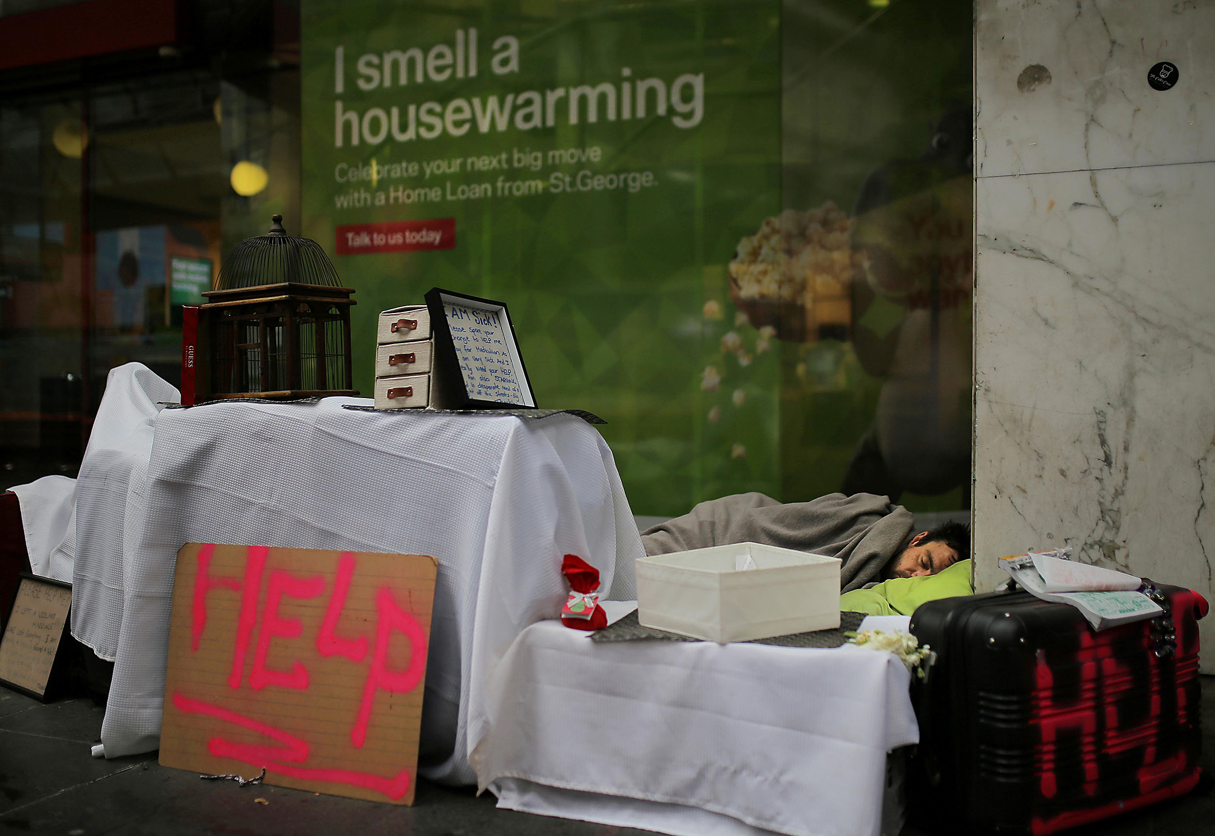  A homeless man sleeps in a makeshift encampment in front of a bank displaying a home loan advertisement in central Sydney, Australia, July 31, 2017. 