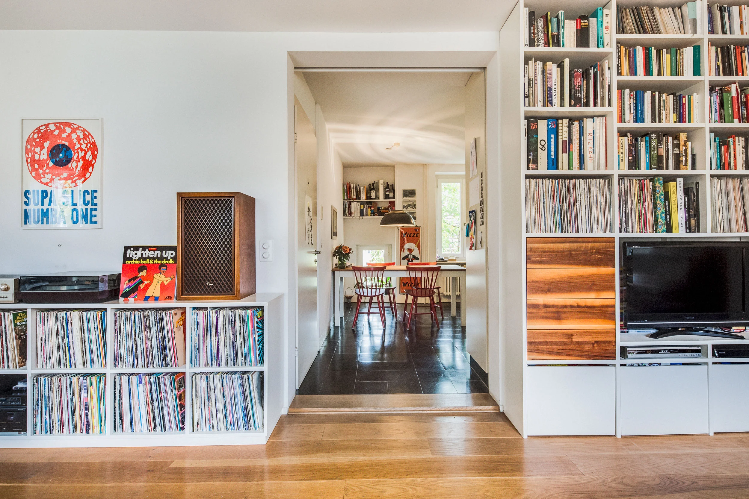 Im Regal mit den durchgehend vertikalen Seiten stehen neben der Vinyl-Sammlung Bücher in unterschiedlichen Formaten. Das weiss lackierte MDF-Regal wurde durch Fronten aus massivem Nussbaum ergänzt, die mit den schlichten Beistelltischchen korrespondieren. Das Eck-Sideboard, beherbergt weitere Schallplatten und bietet Platz für das Hi-Fi Soundsystem.